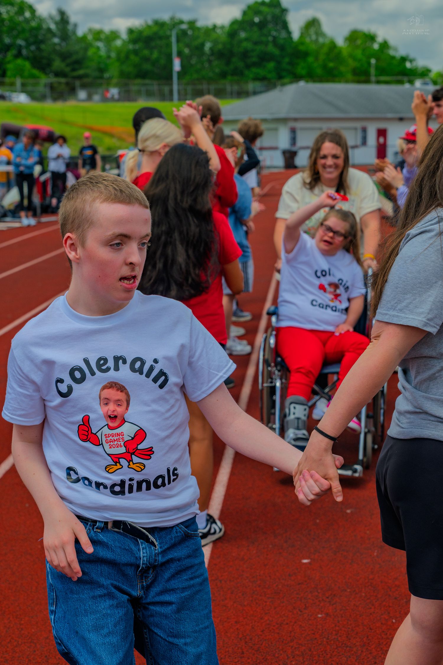 Students in Colerain Cardinals shirts participate in a Special Olympics track event on a red running track.