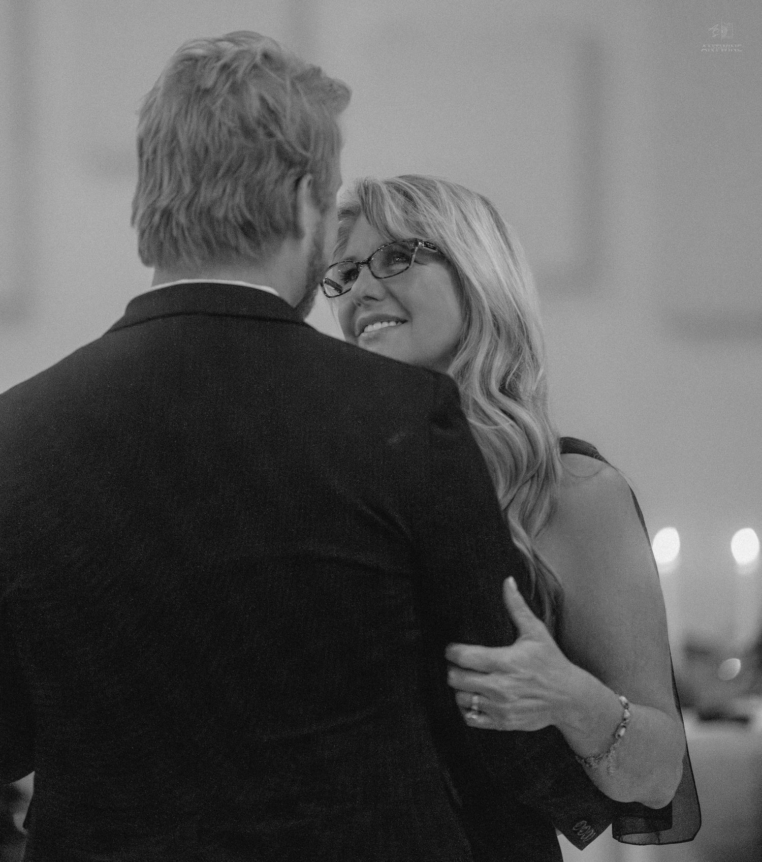Black and white photo of a couple sharing a romantic dance, woman smiling warmly wearing glasses and bracelet.