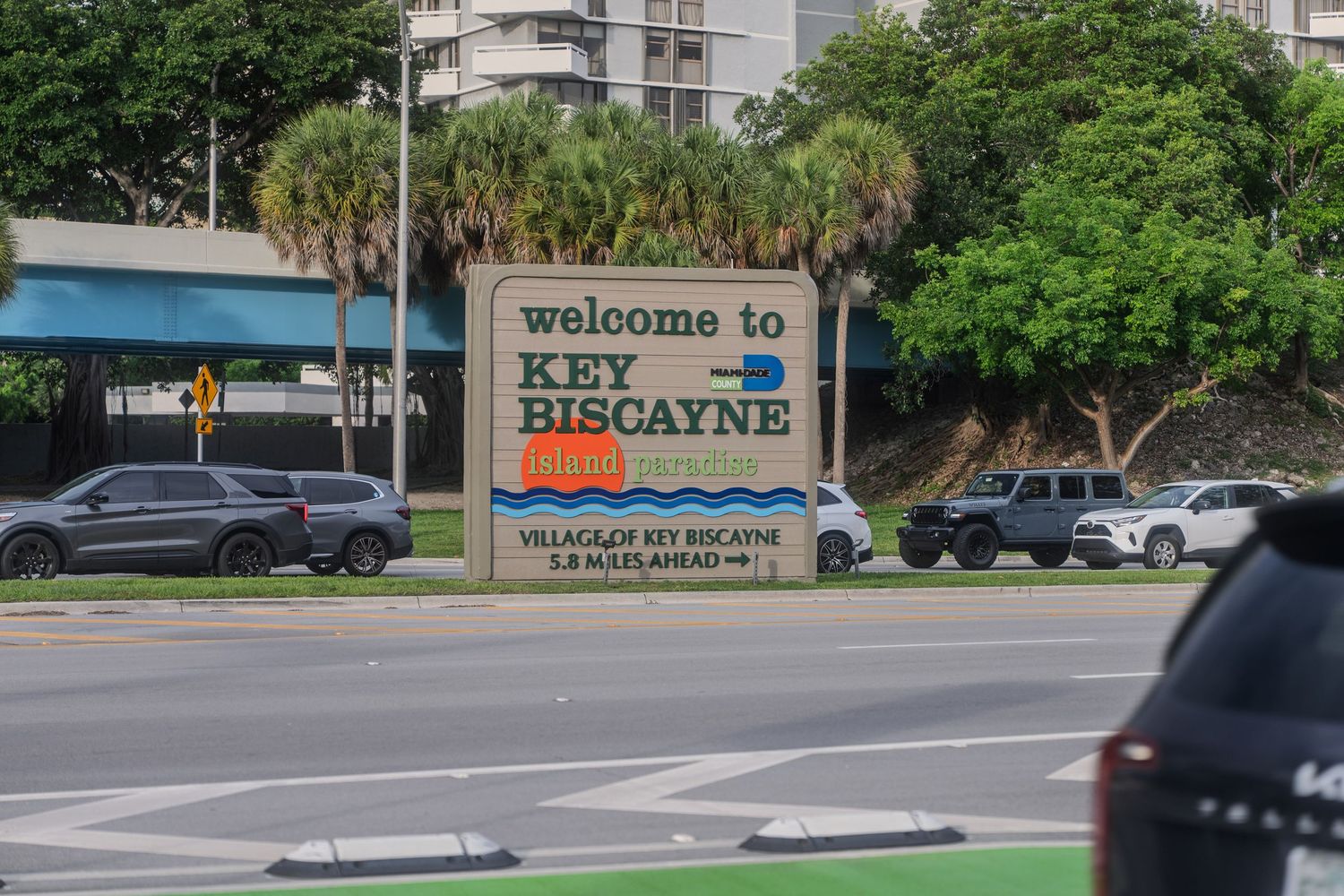 Welcome to Key Biscayne village sign on a sunny day with palm trees and traffic in Miami, Florida.