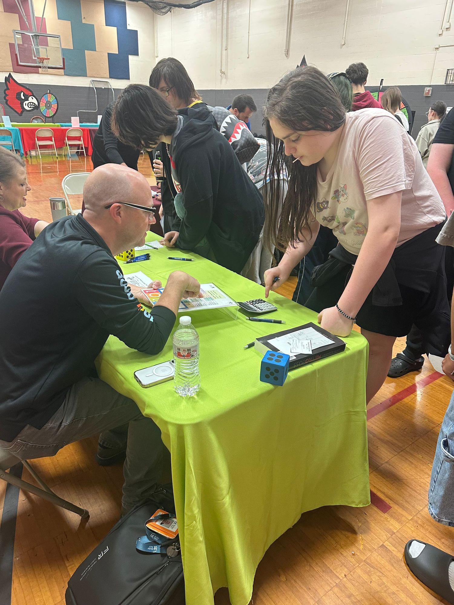 Students interact with a recruiter at a green table during a school career fair in a gymnasium.
