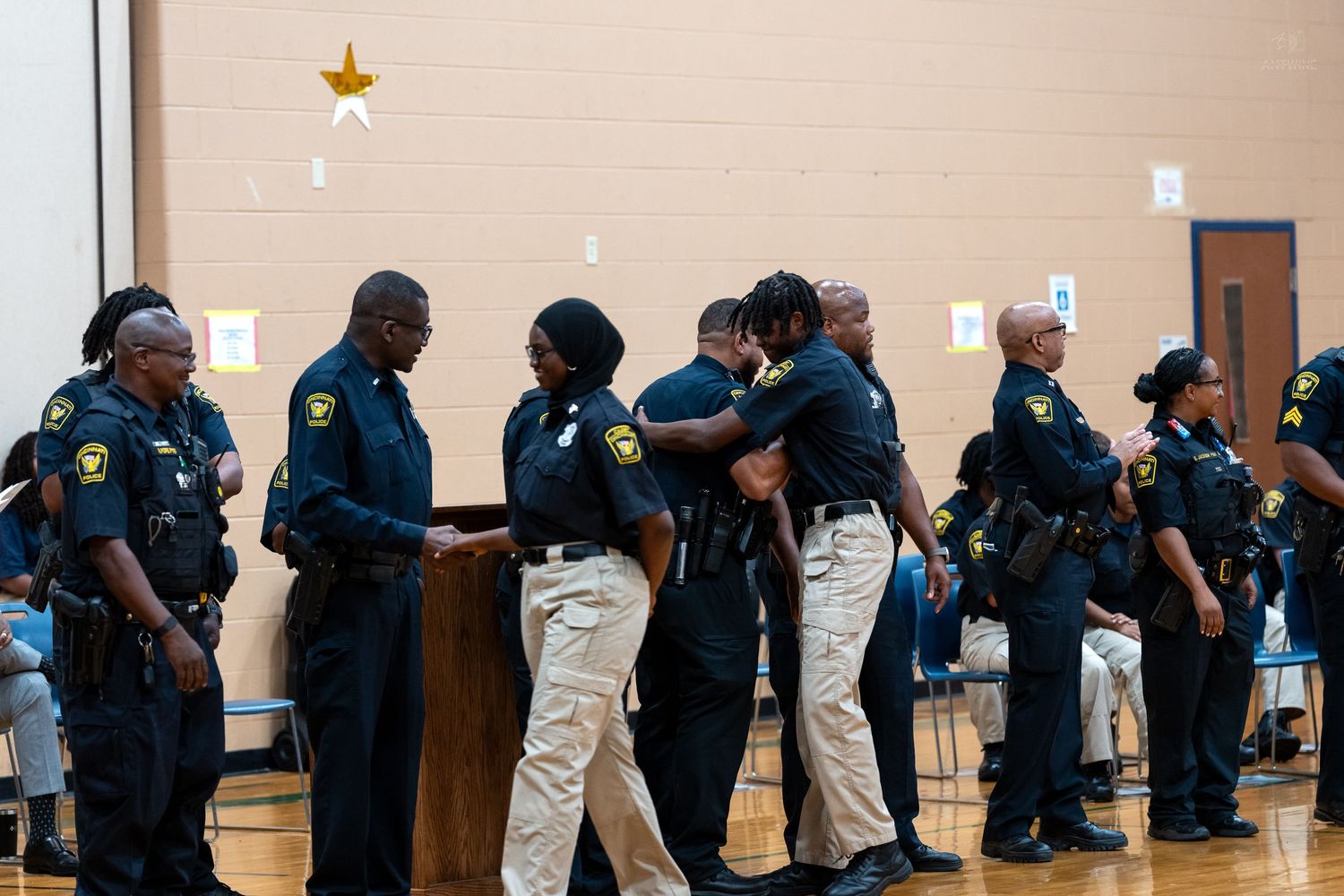 Black police officers share a congratulatory hug during an indoor badge pinning or graduation ceremony.