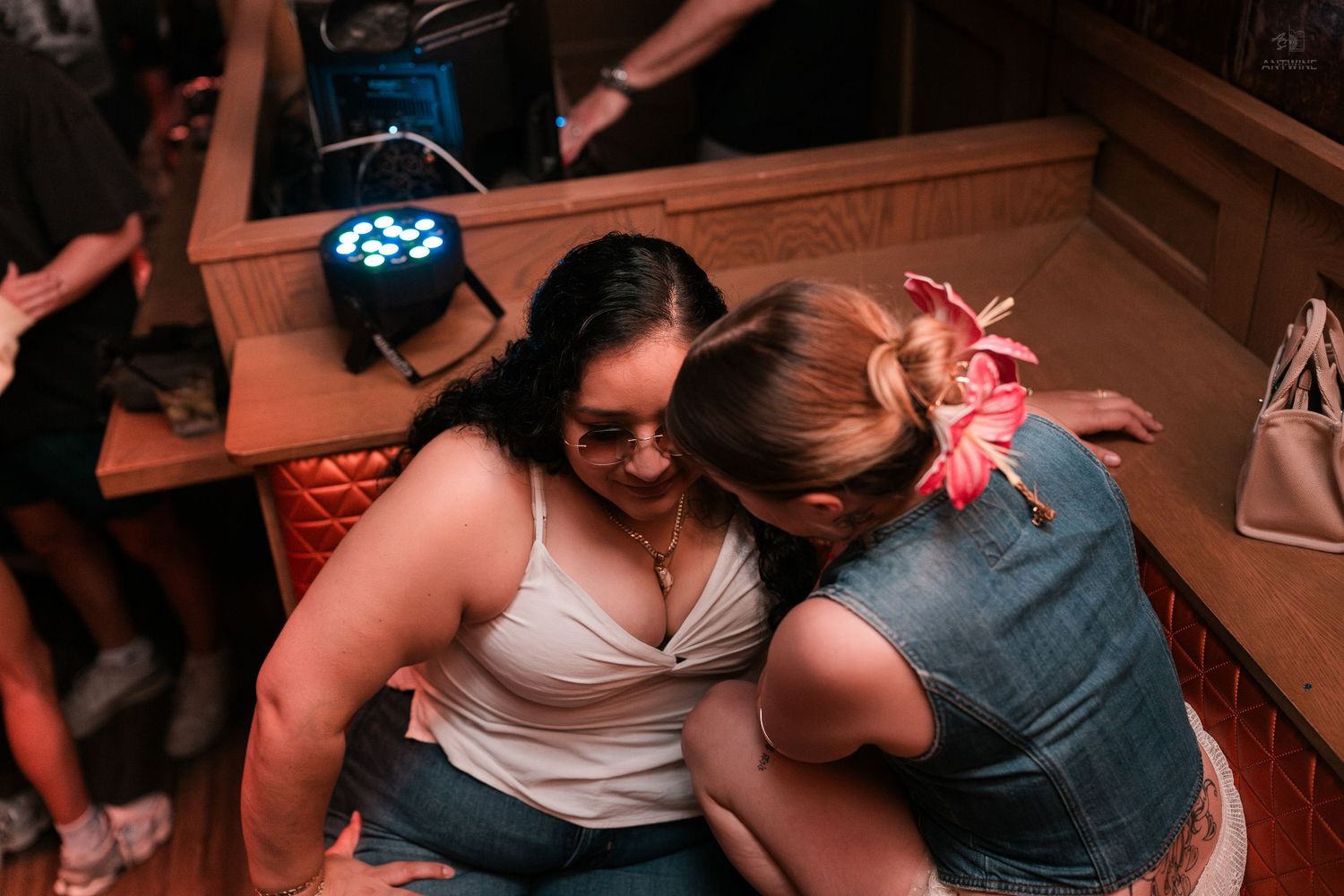 Two women share a close moment together while seated at a lively indoor bar or nightclub event.