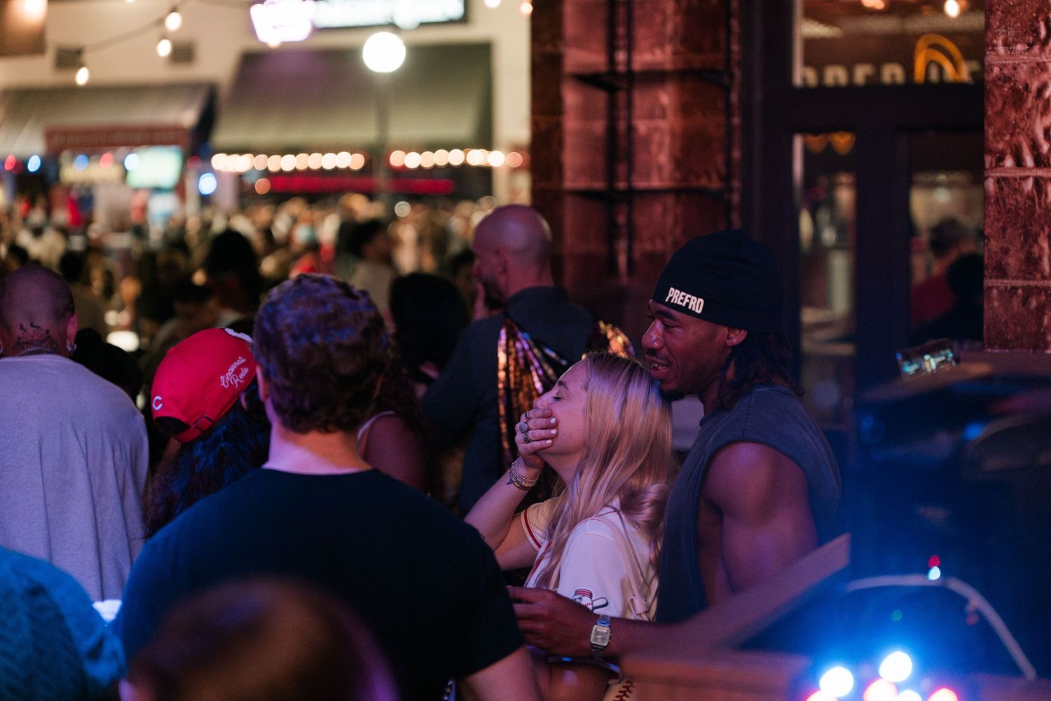 Couple embracing outside a busy nightclub entrance illuminated by colorful lights.