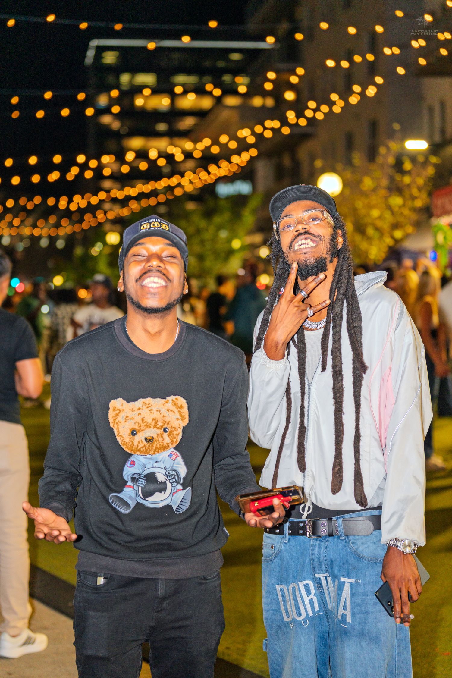 Two men smiling and posing under string lights at an outdoor night event.