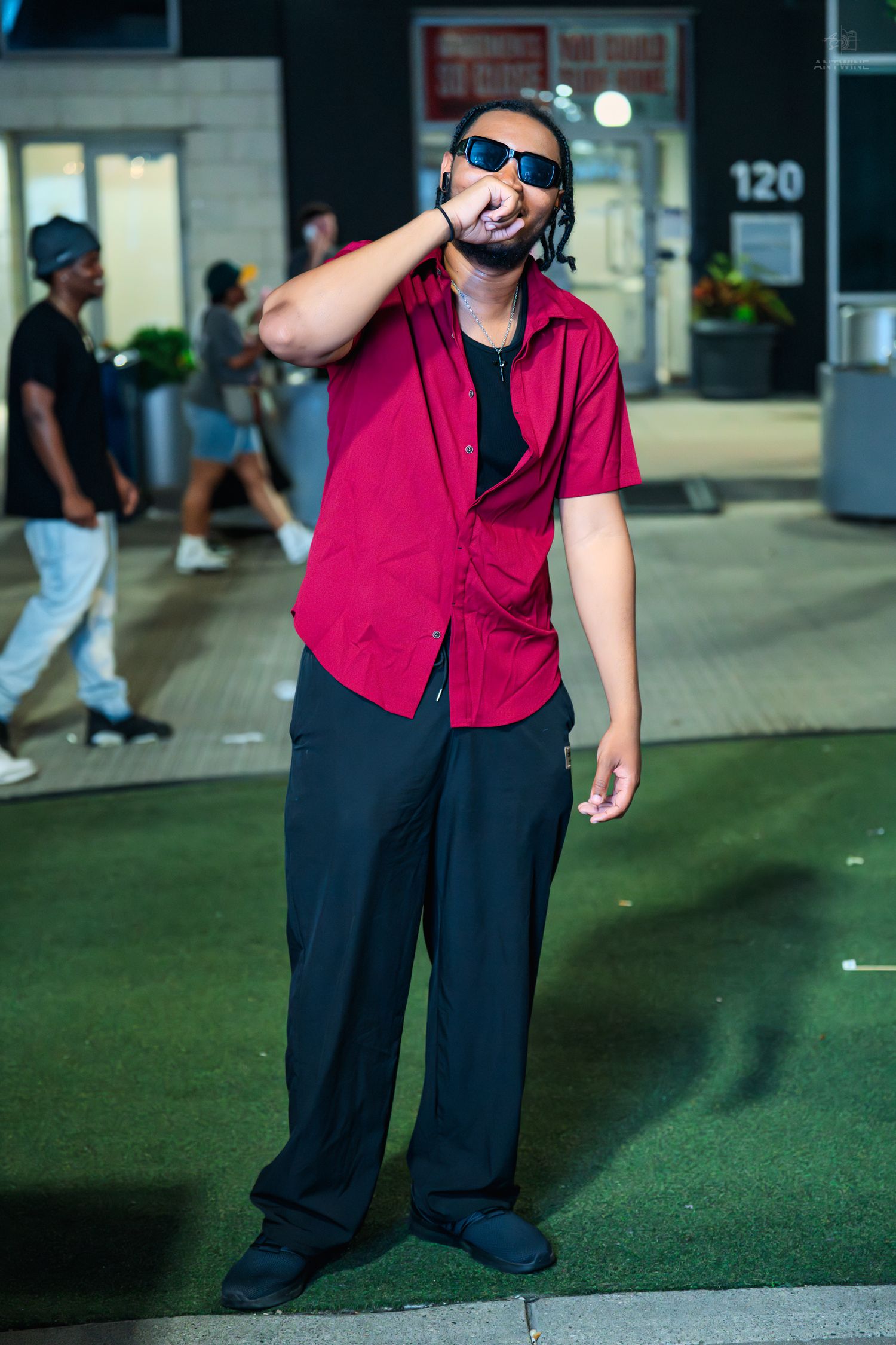 Man in red shirt and sunglasses posing outdoors at night near building 120.