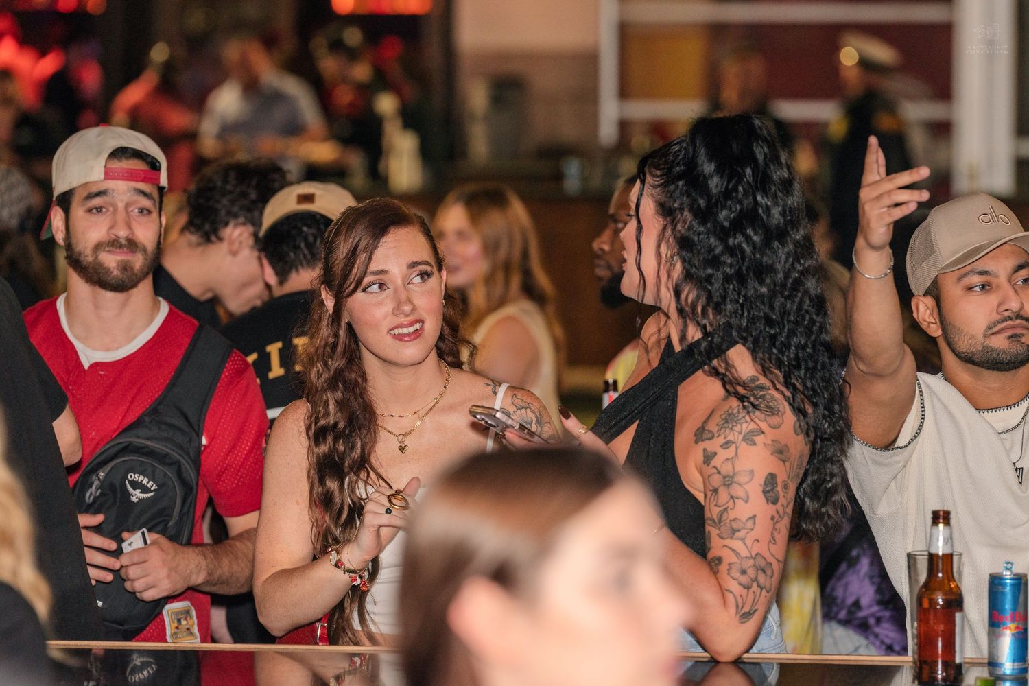 Group of young adults socializing and chatting at a busy indoor bar or nightclub event.