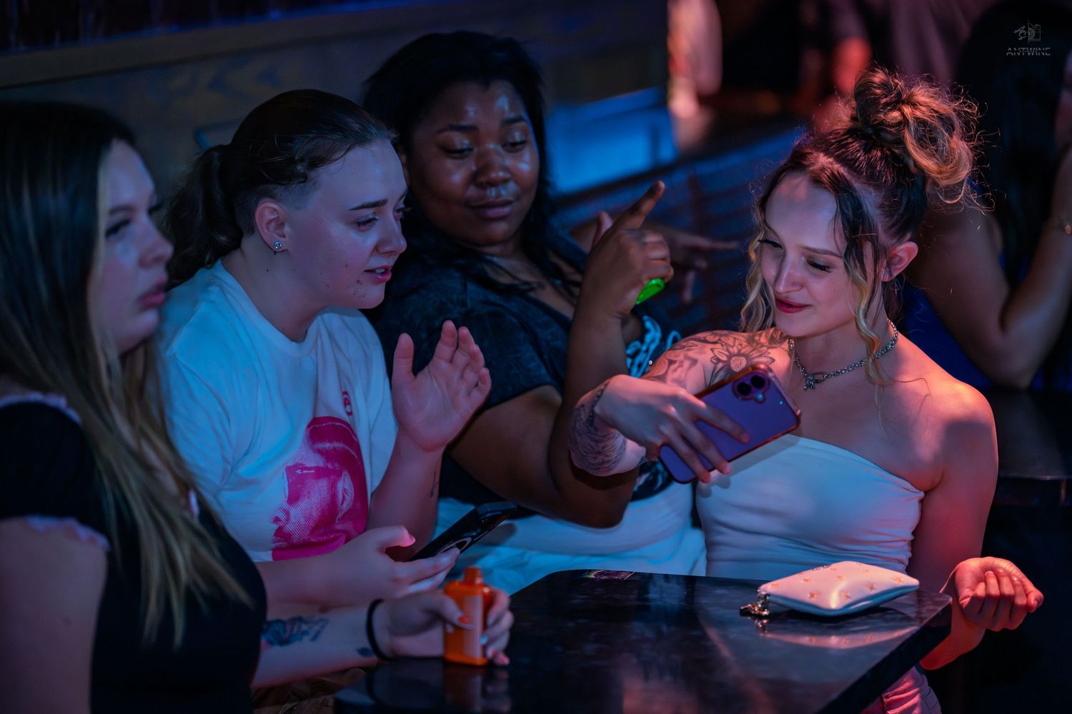 Group of four women gathered around a table at a vibrant nightclub event.