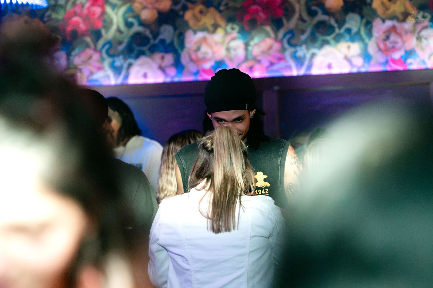 Person in black beanie in intimate moment amid nightclub crowd.
