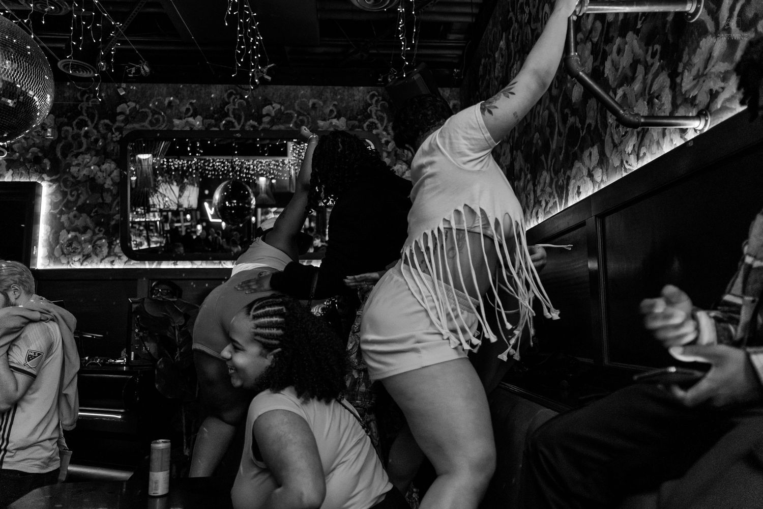 Woman in fringed outfit dancing on a bar counter at a lively nightclub party.