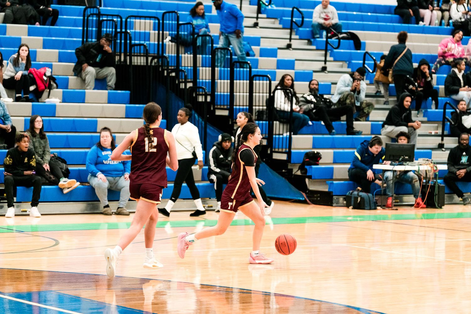 Two Turpin girls basketball players in maroon uniforms advance the ball downcourt during a high school basketball game.