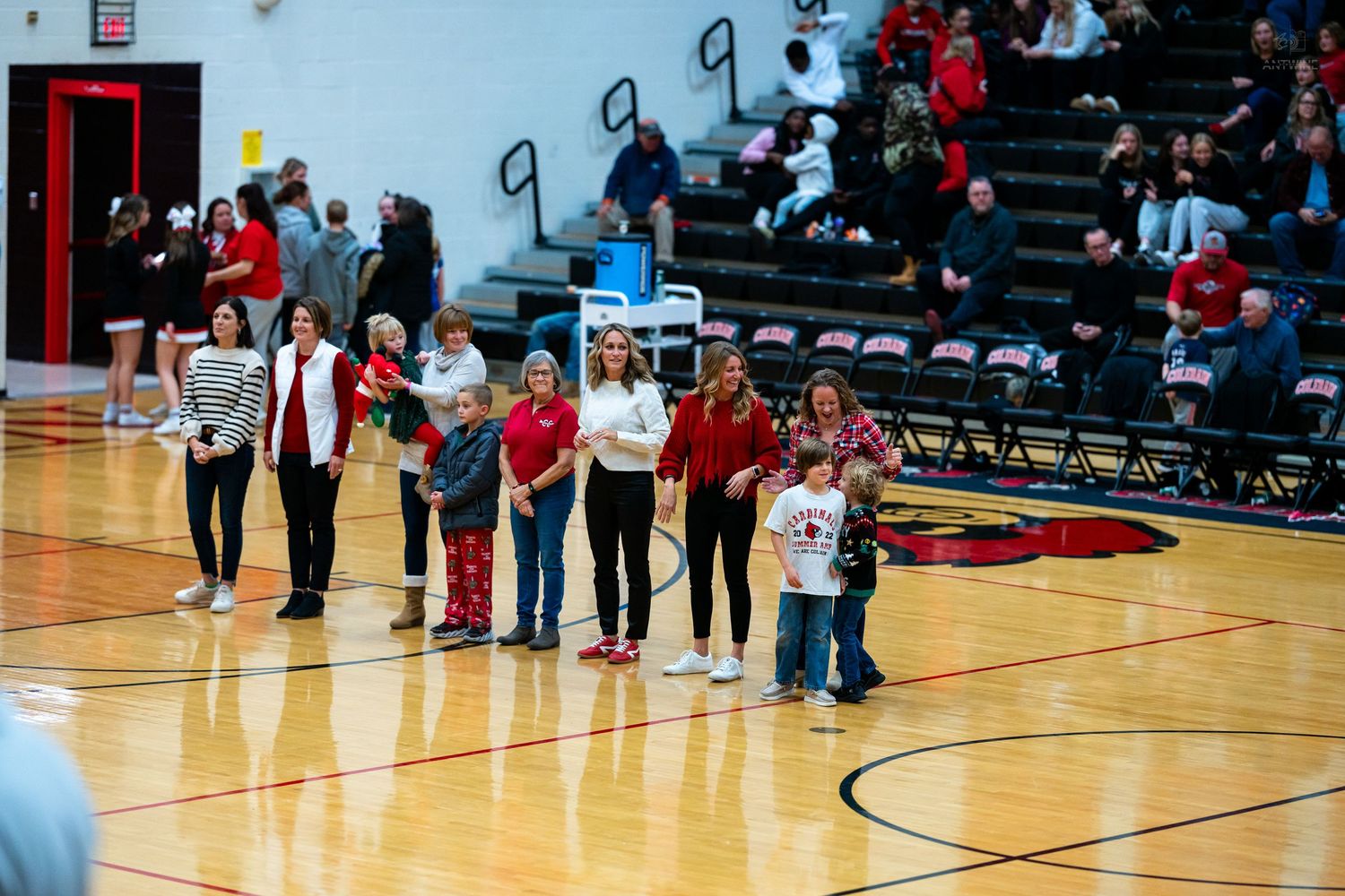 Group of people stand on a basketball court floor during a recognition ceremony before a packed gymnasium crowd.