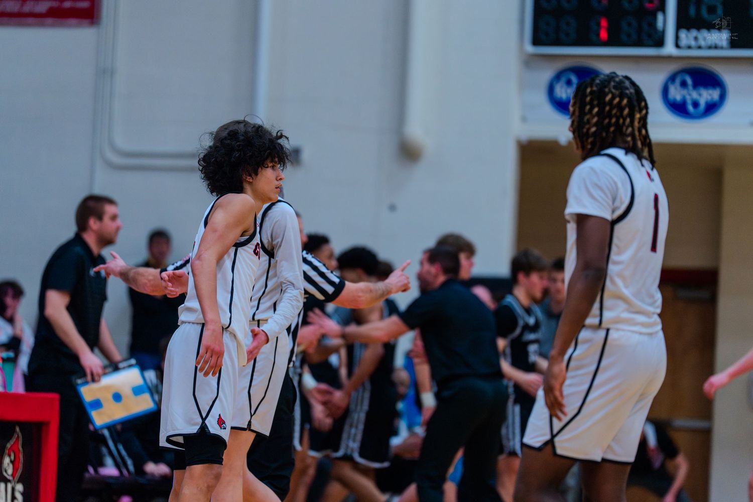 Two basketball players in white uniforms walk off court during a high school basketball game.