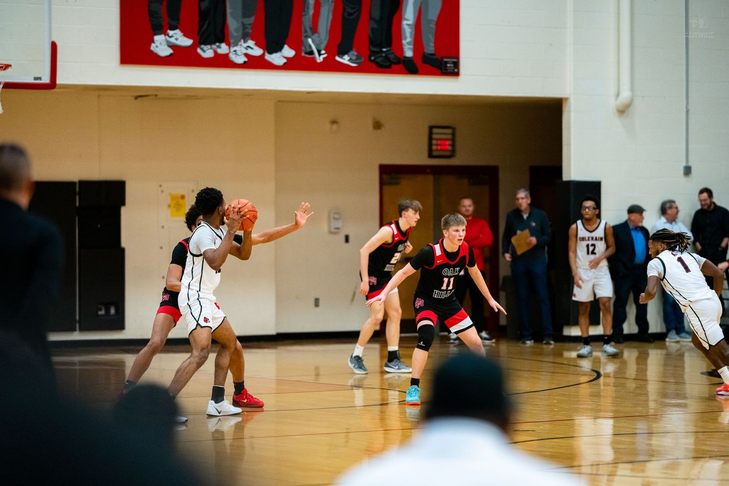 Colerain Cardinals basketball player drives against defenders during packed high school gymnasium game.