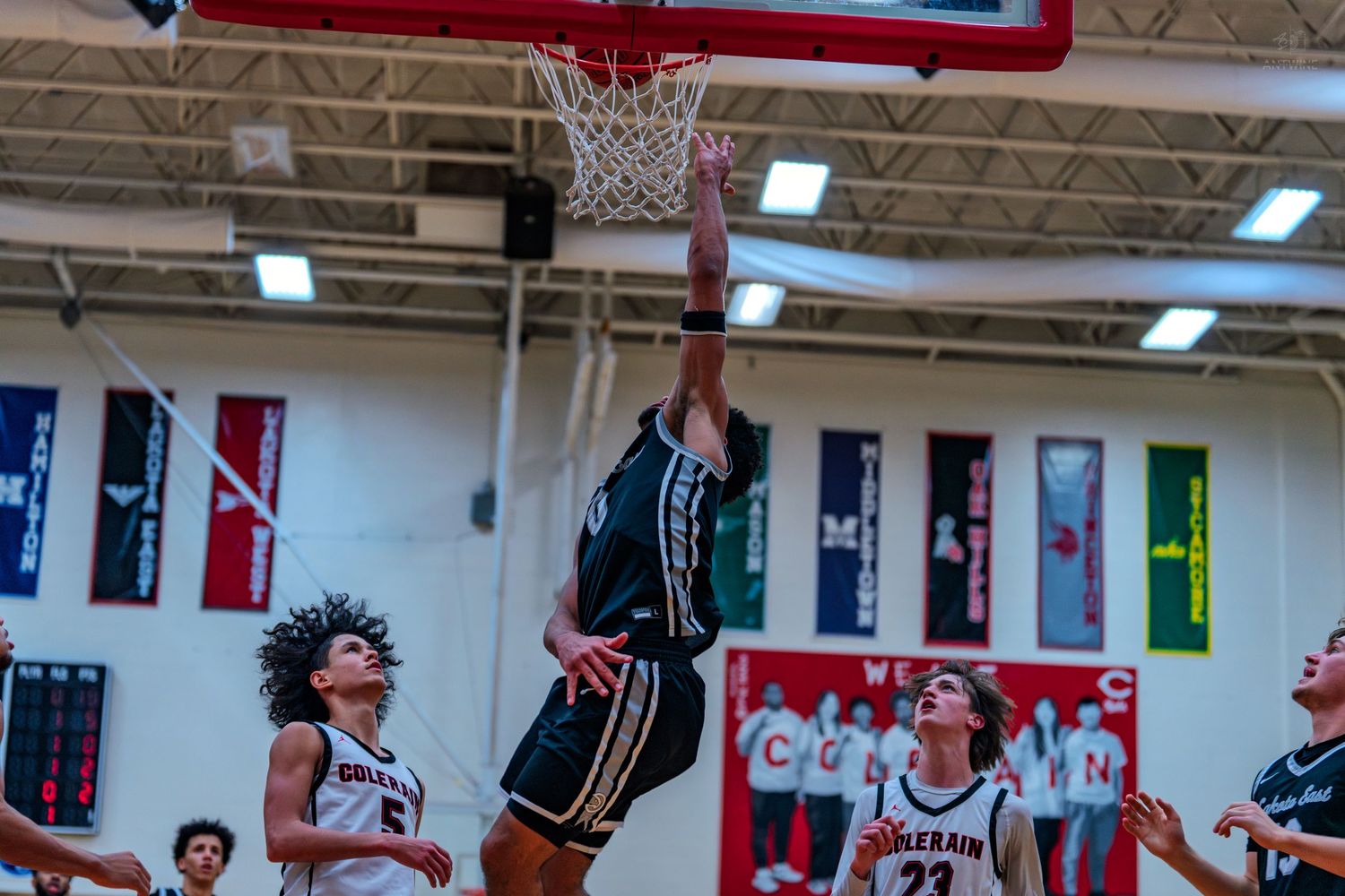Athletic basketball player in teal jersey executes dramatic slam dunk during high school gymnasium game.