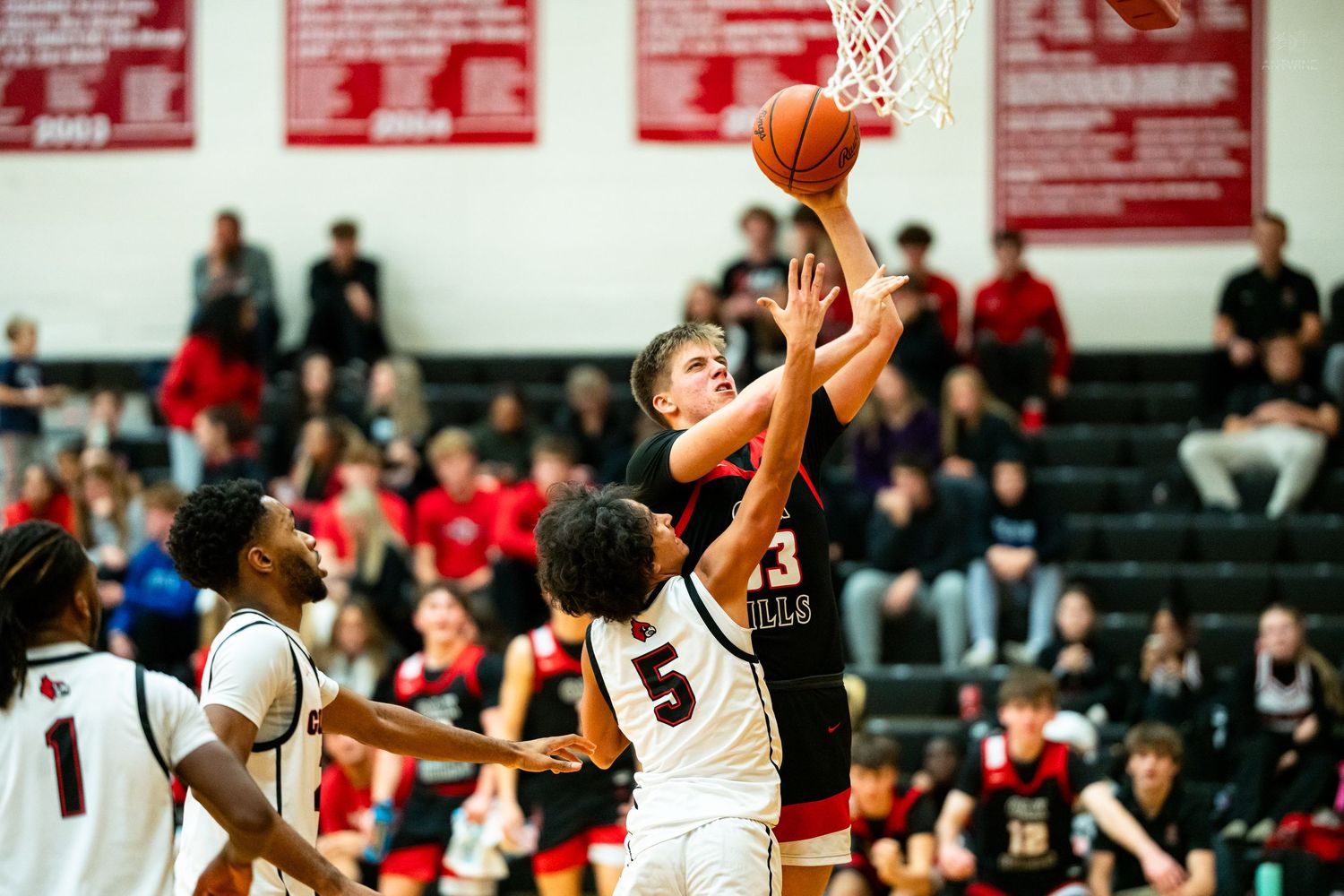 A basketball player goes up for a layup against a defender during a packed high school gym game.