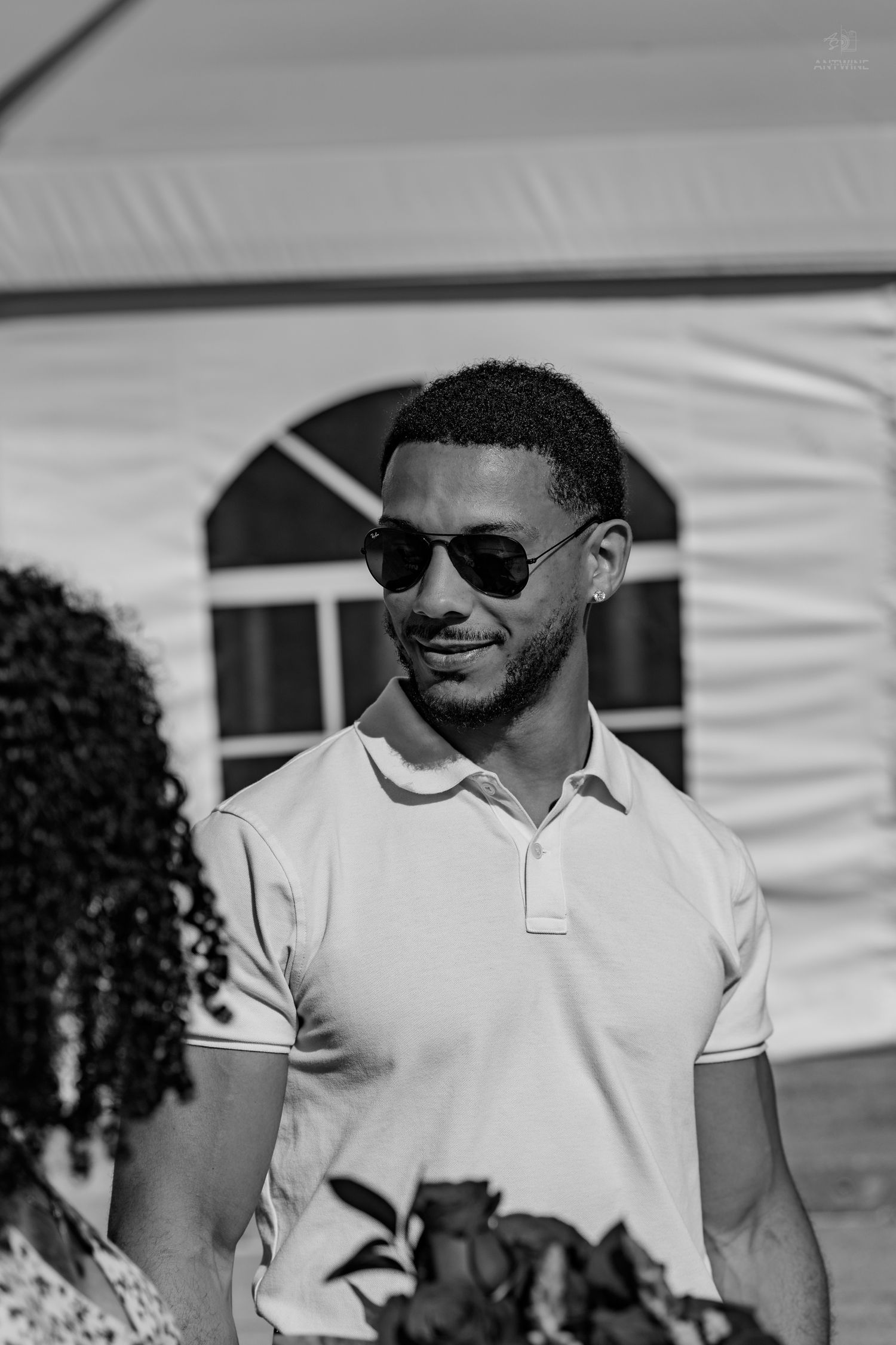 Black and white photo of a young man in sunglasses and white polo shirt smiling near a white event tent.