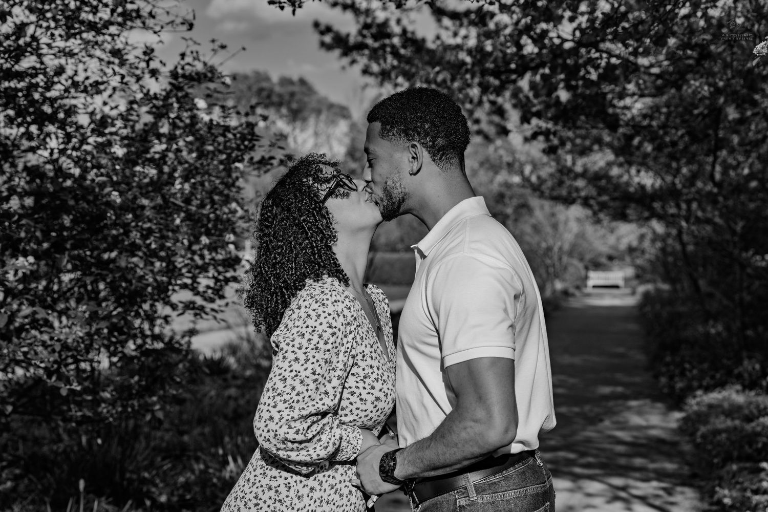 Romantic Black couple sharing a kiss while embracing outdoors in a black and white photo.