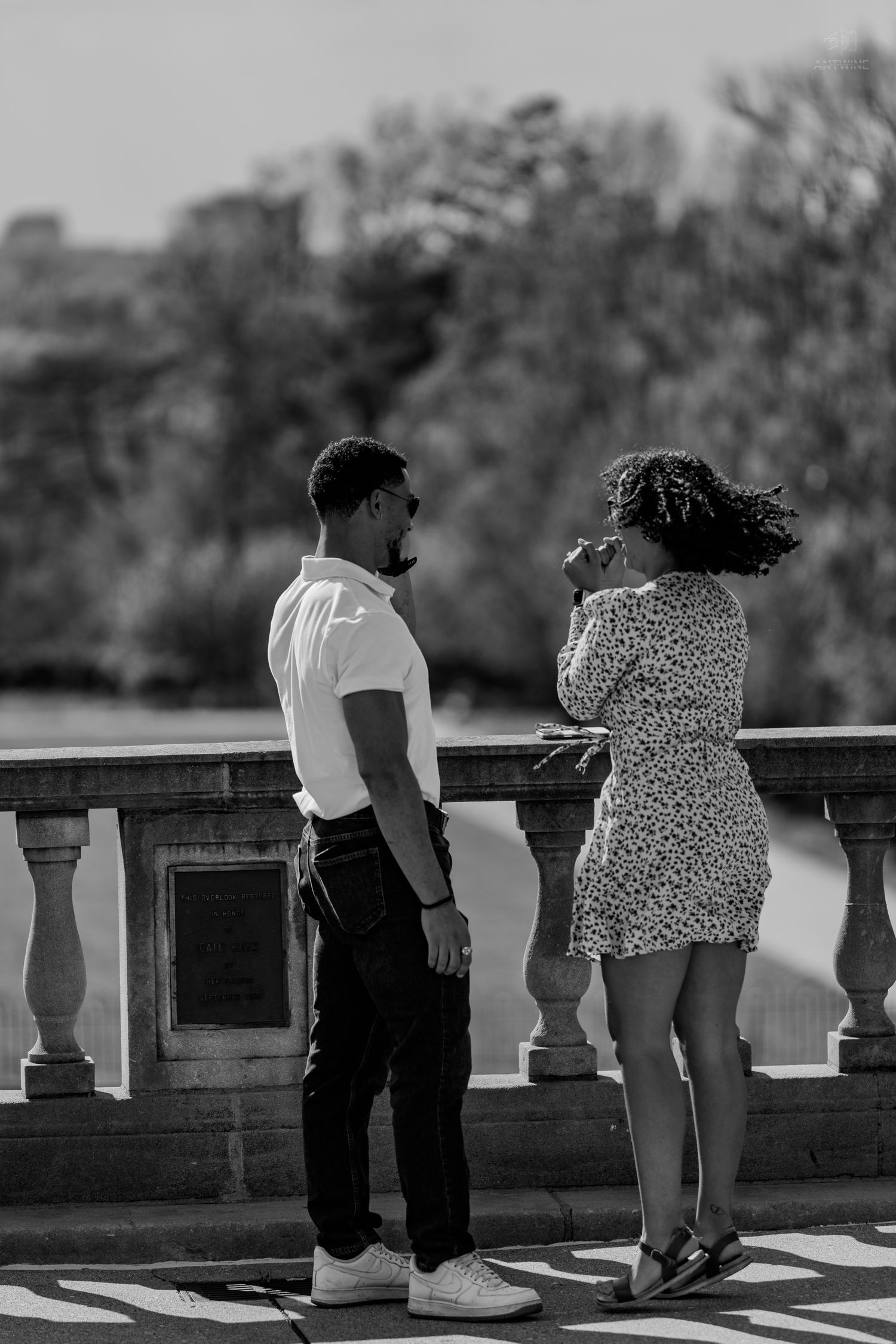 Black and white photo of a couple standing closely together on a scenic outdoor stone balcony.