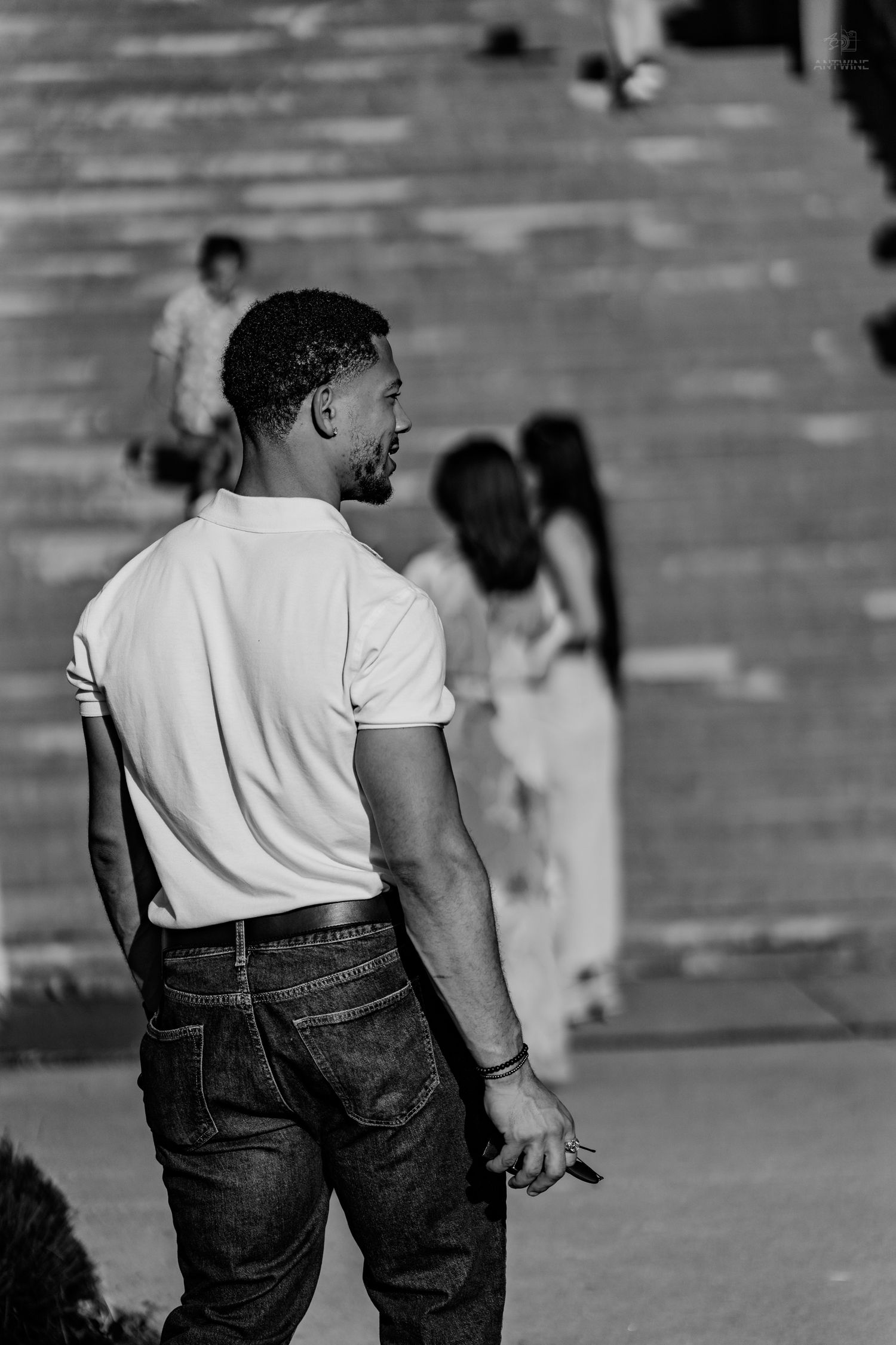 A young Black man in a white t-shirt and jeans stands with his back to the camera on outdoor steps.
