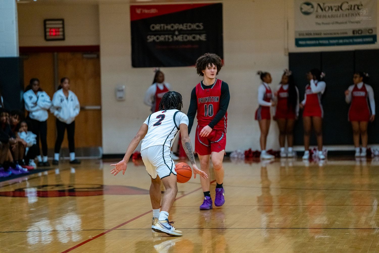 Basketball player in red jersey dribbles against defender in white during indoor high school game.