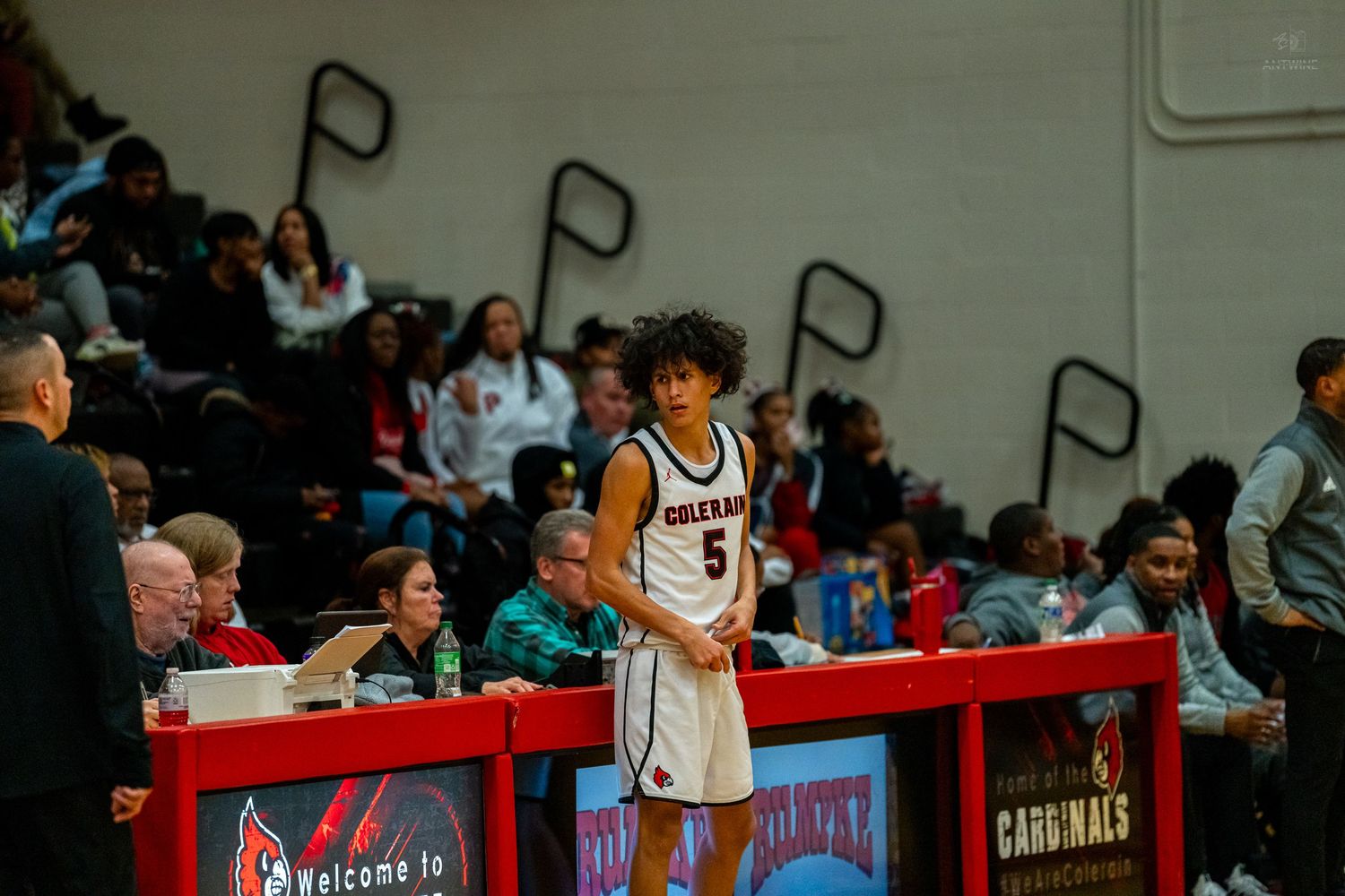 Player #5 in white Colerain jersey stands at scorer's table during high school basketball game.