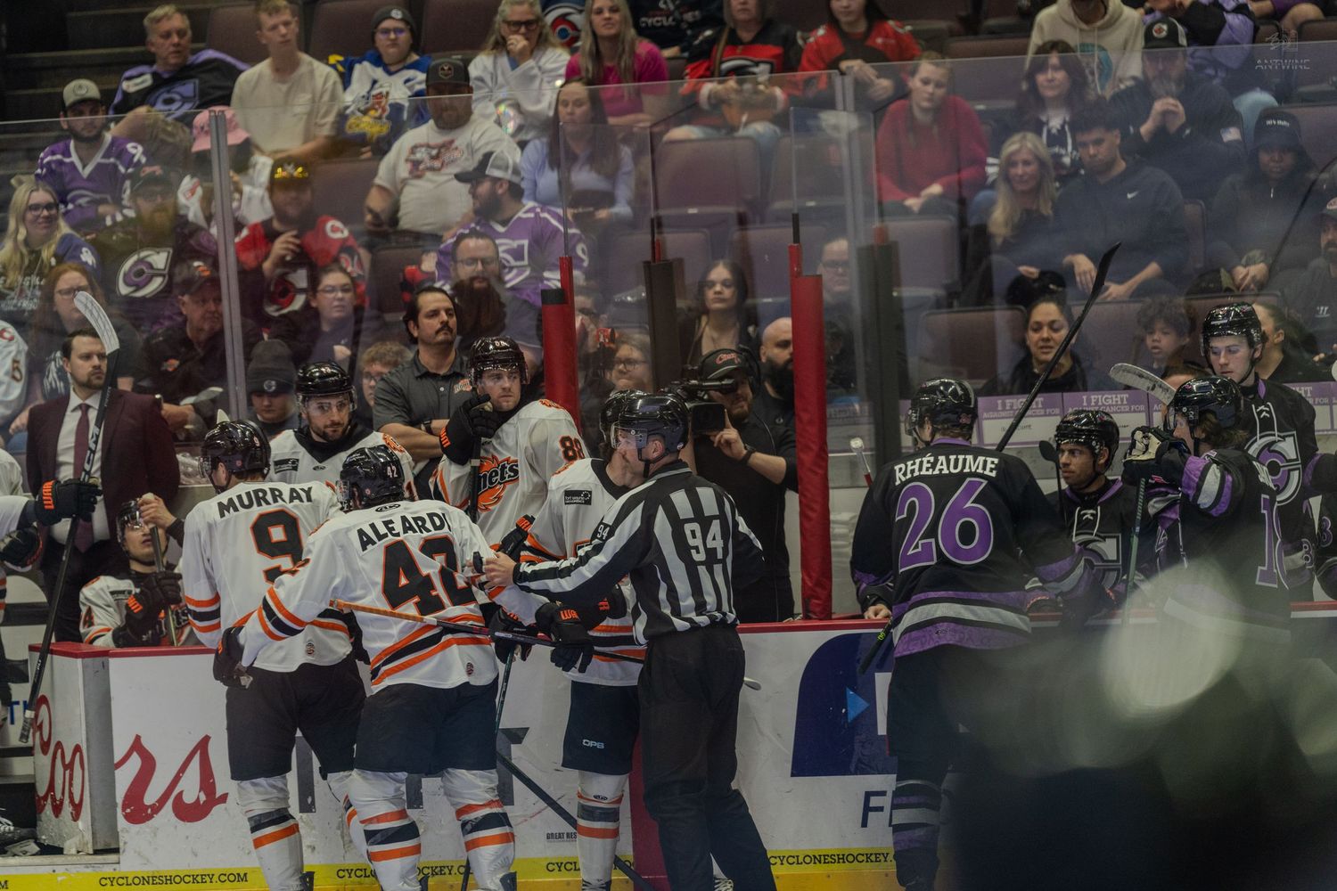 Ice hockey players and referee gather in scrum near boards during heated professional hockey game moment.