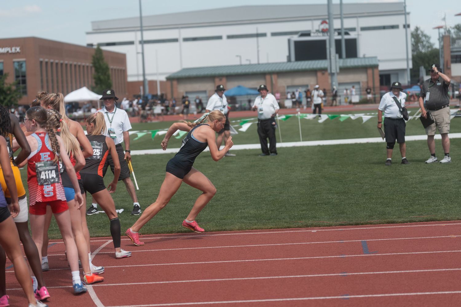 Female relay runner crouches in starting position awaiting a baton pass at a high school state track meet.