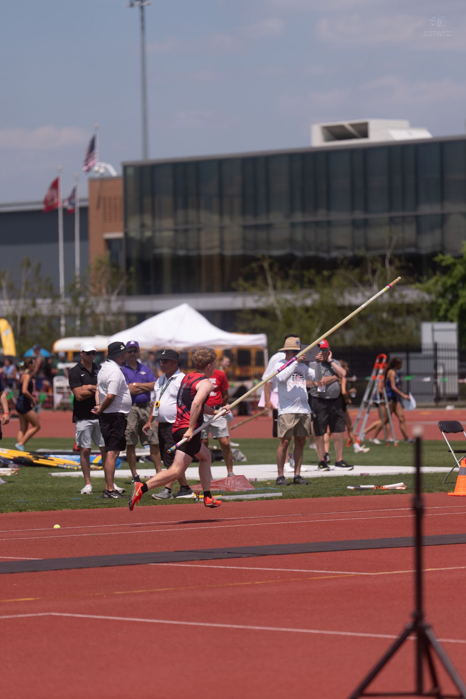 Young athlete runs down the track carrying a javelin at an outdoor track and field competition.