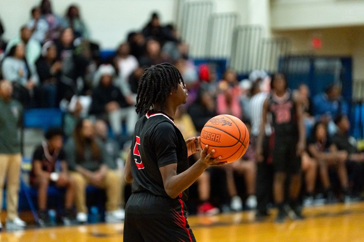 A basketball player in black and red uniform prepares to shoot during a high school basketball game.