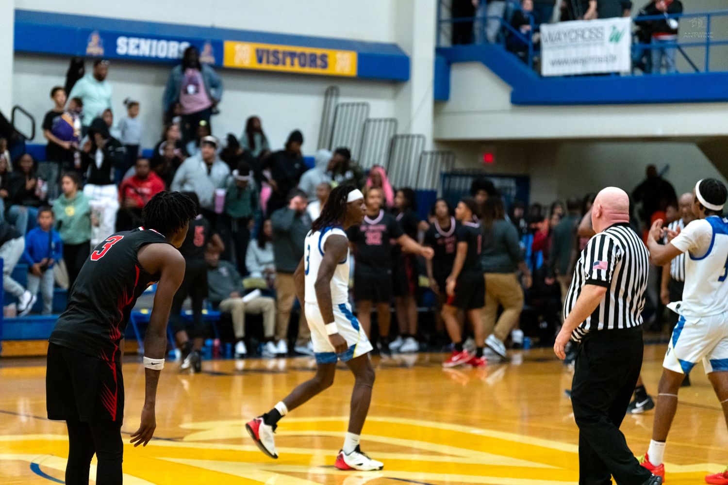 Northwest Knights player celebrates on court near referee while opposing team players react during a high school basketball game.