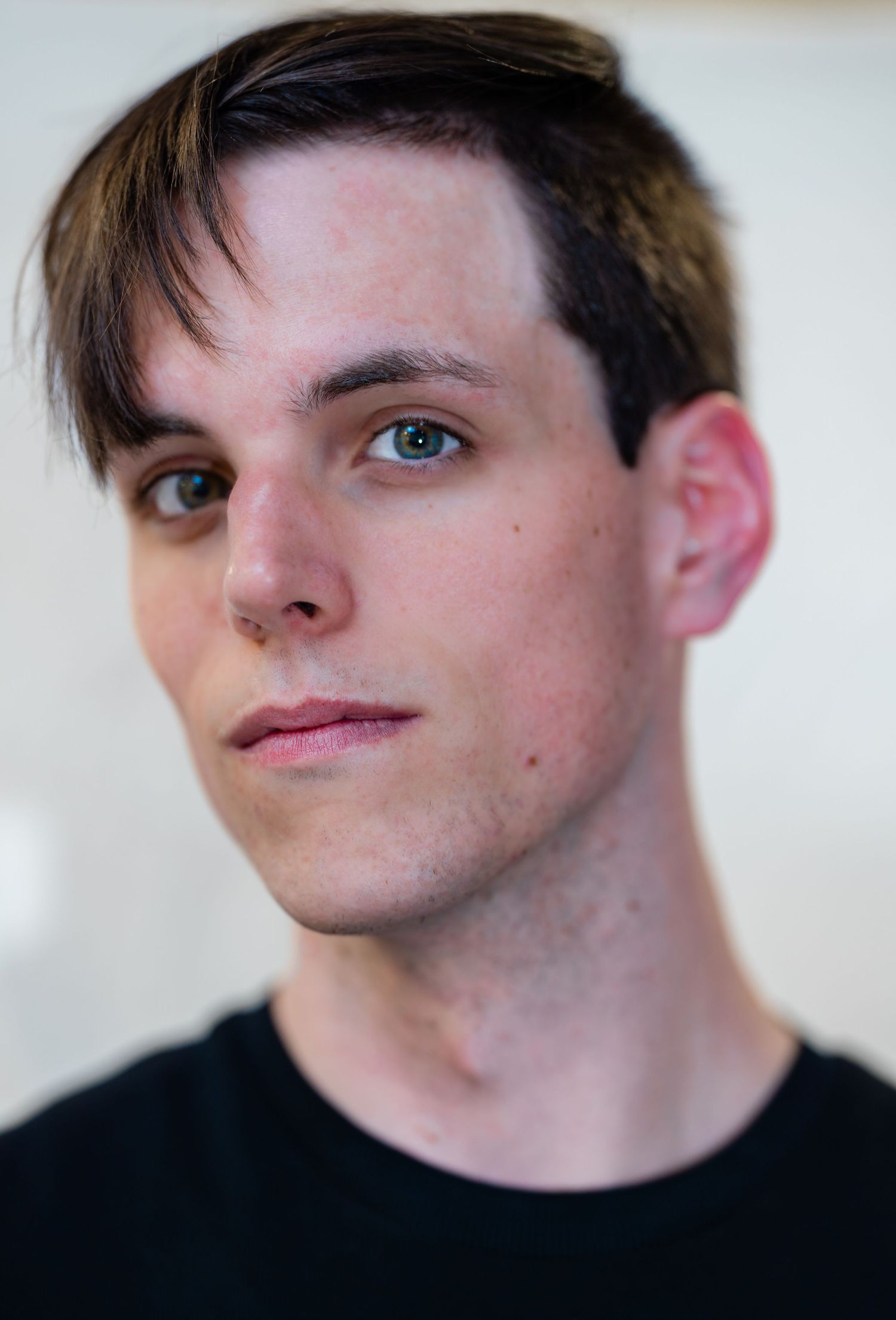 Young man with dark hair and blue eyes wearing a black t-shirt poses for a professional headshot photo.