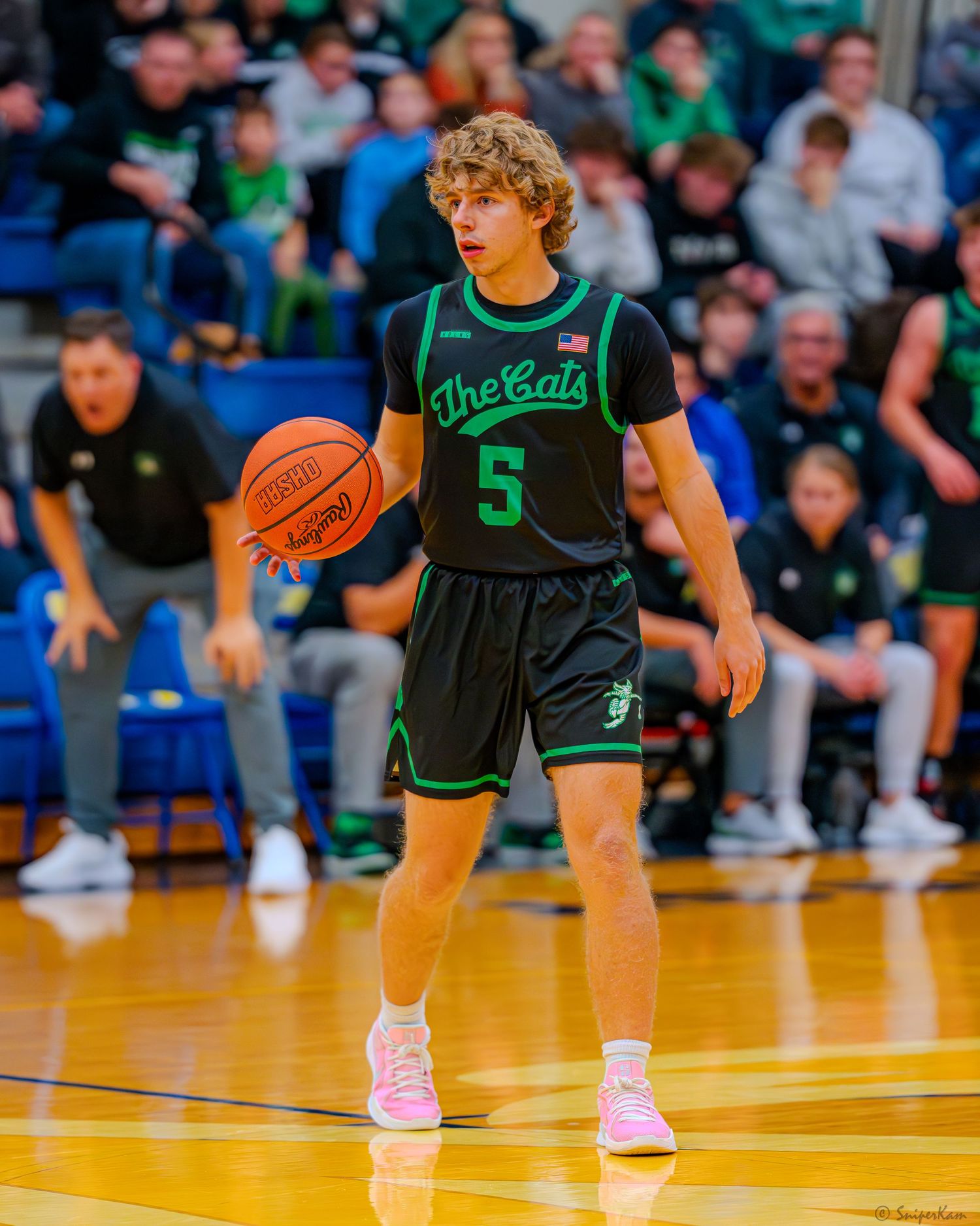 Young basketball player in black Cats jersey number 5 dribbling during indoor game.