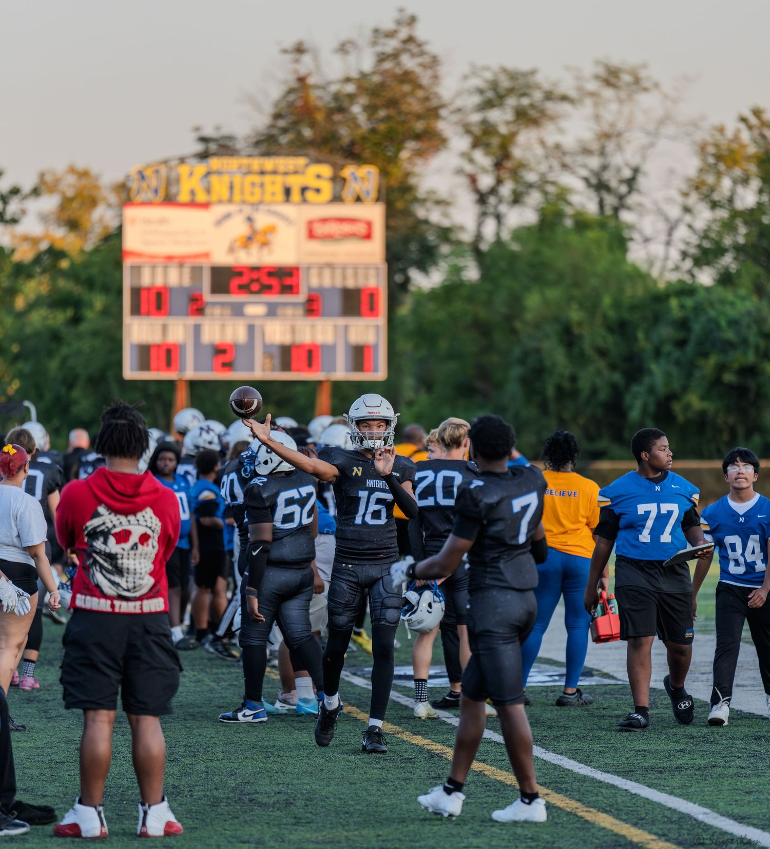 Football players warm up on a field in front of a Knights scoreboard at dusk.