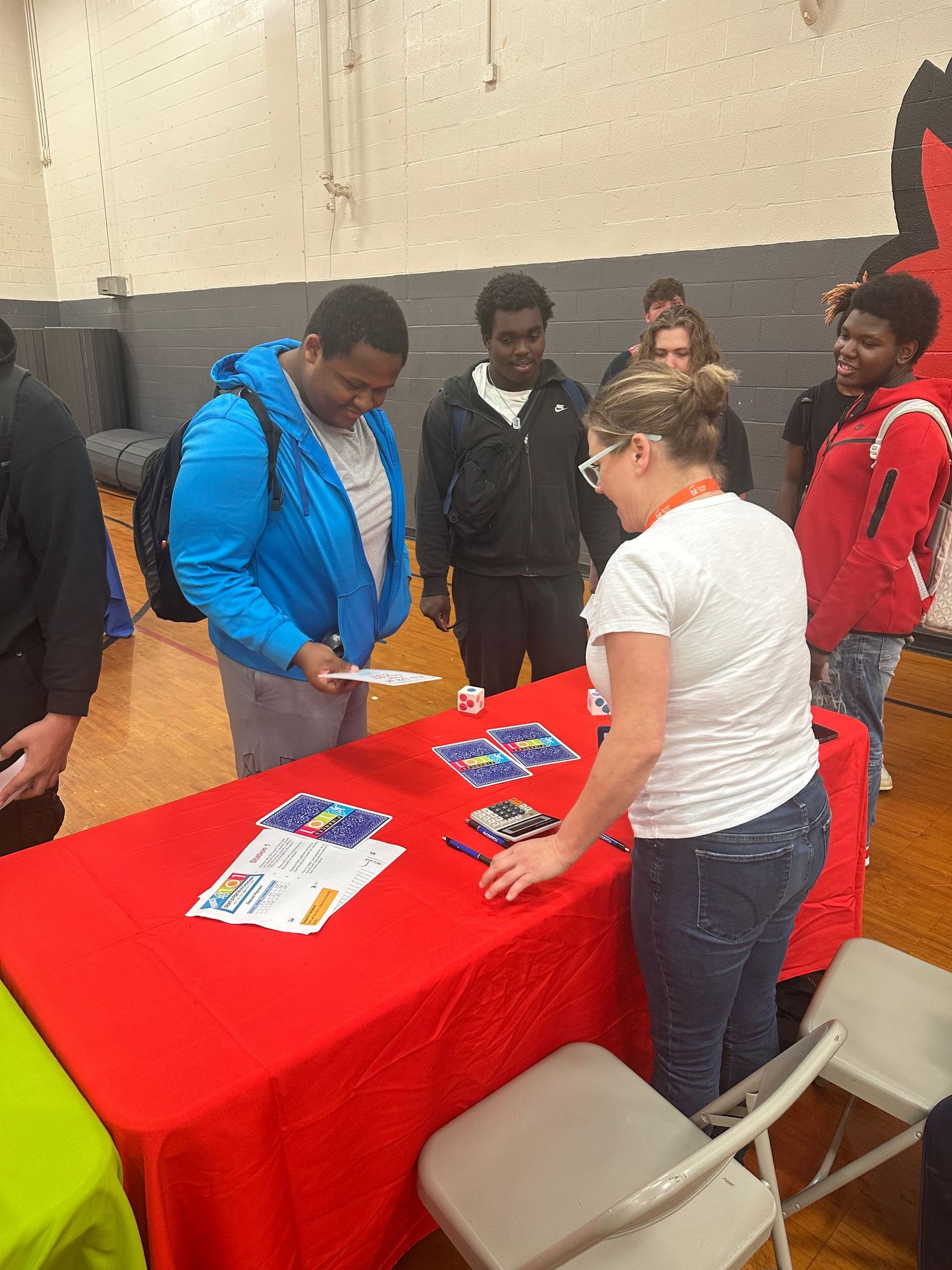 A student reviews materials with a recruiter at a red table during a high school career fair event.