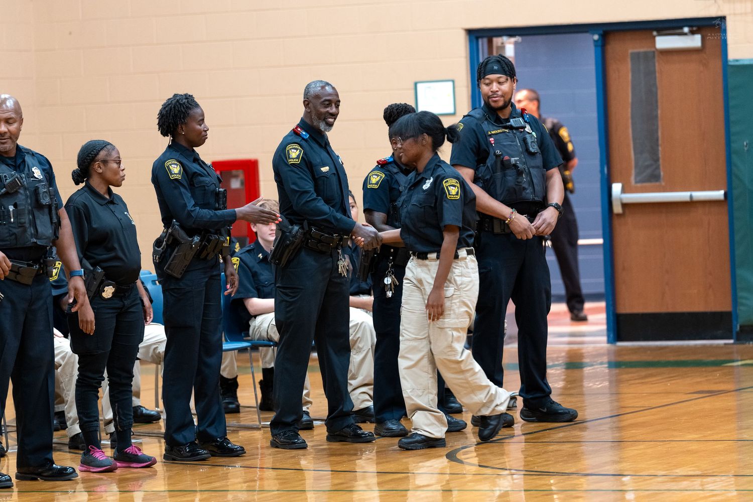 Law enforcement officers in uniform standing in a line during a school gymnasium ceremony or event.