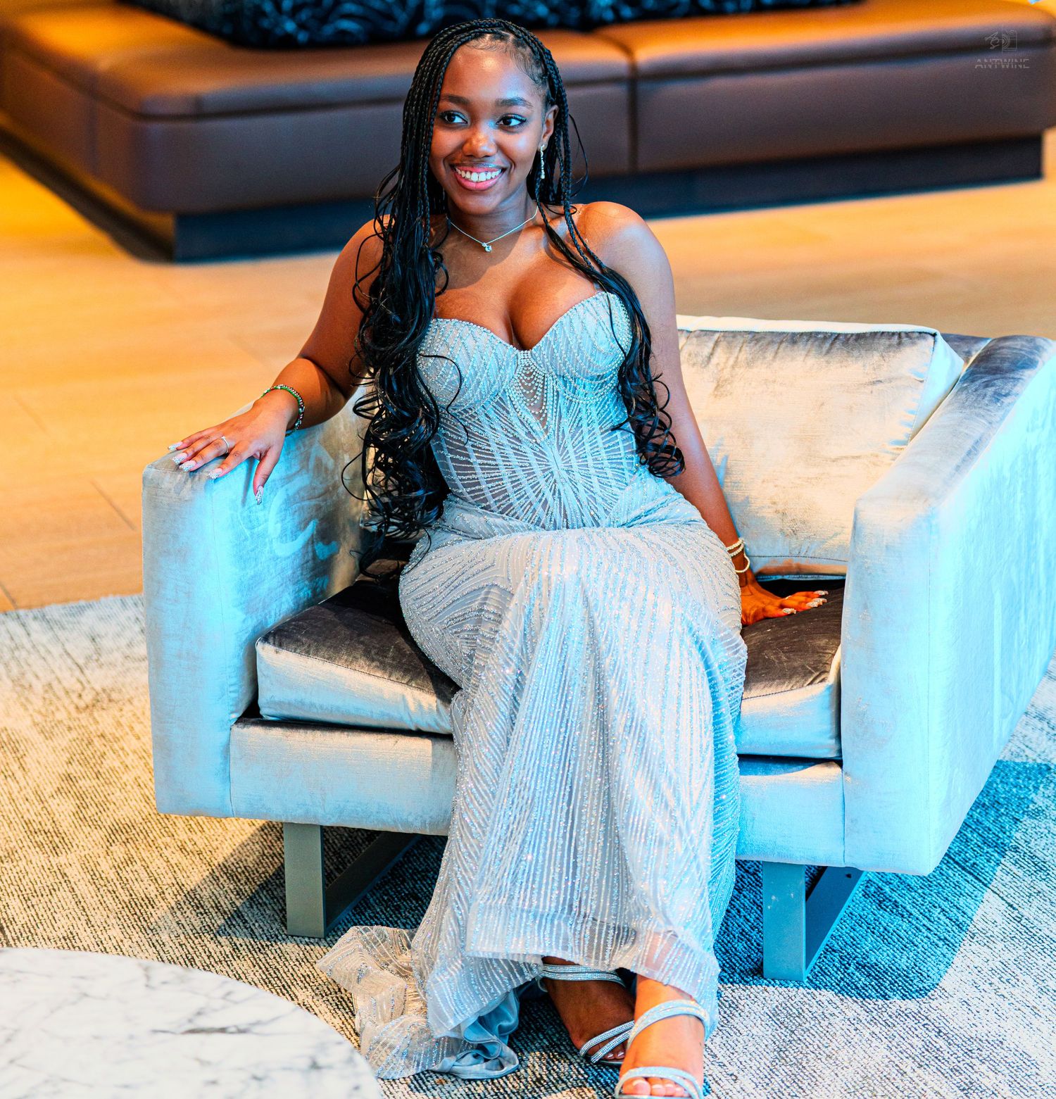 Woman in silver sequin gown sitting elegantly on a modern chair, smiling confidently at a formal event.