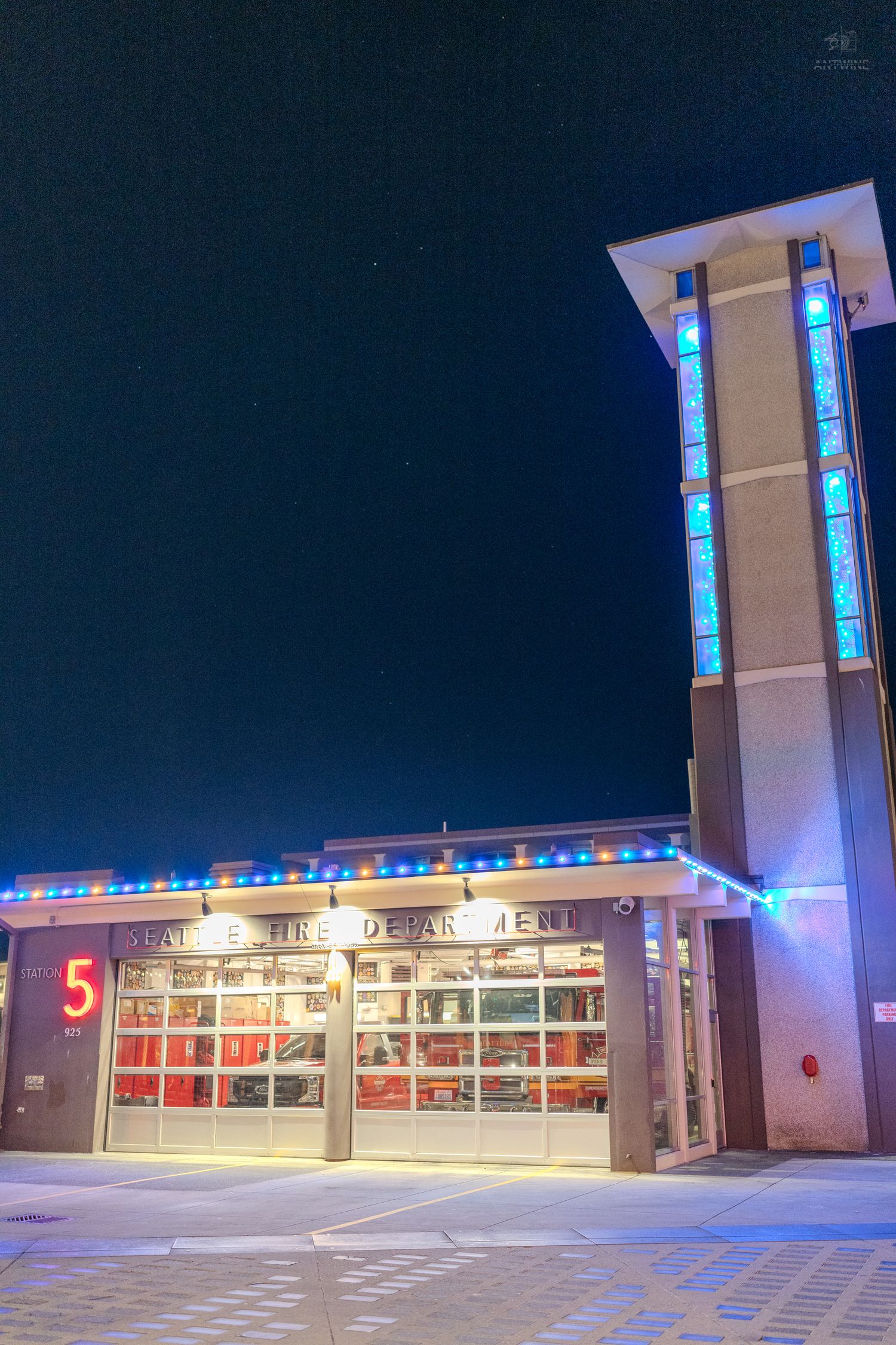 Fire Station 5 illuminated with colorful holiday lights at night, featuring a modern tower with blue stained glass windows.