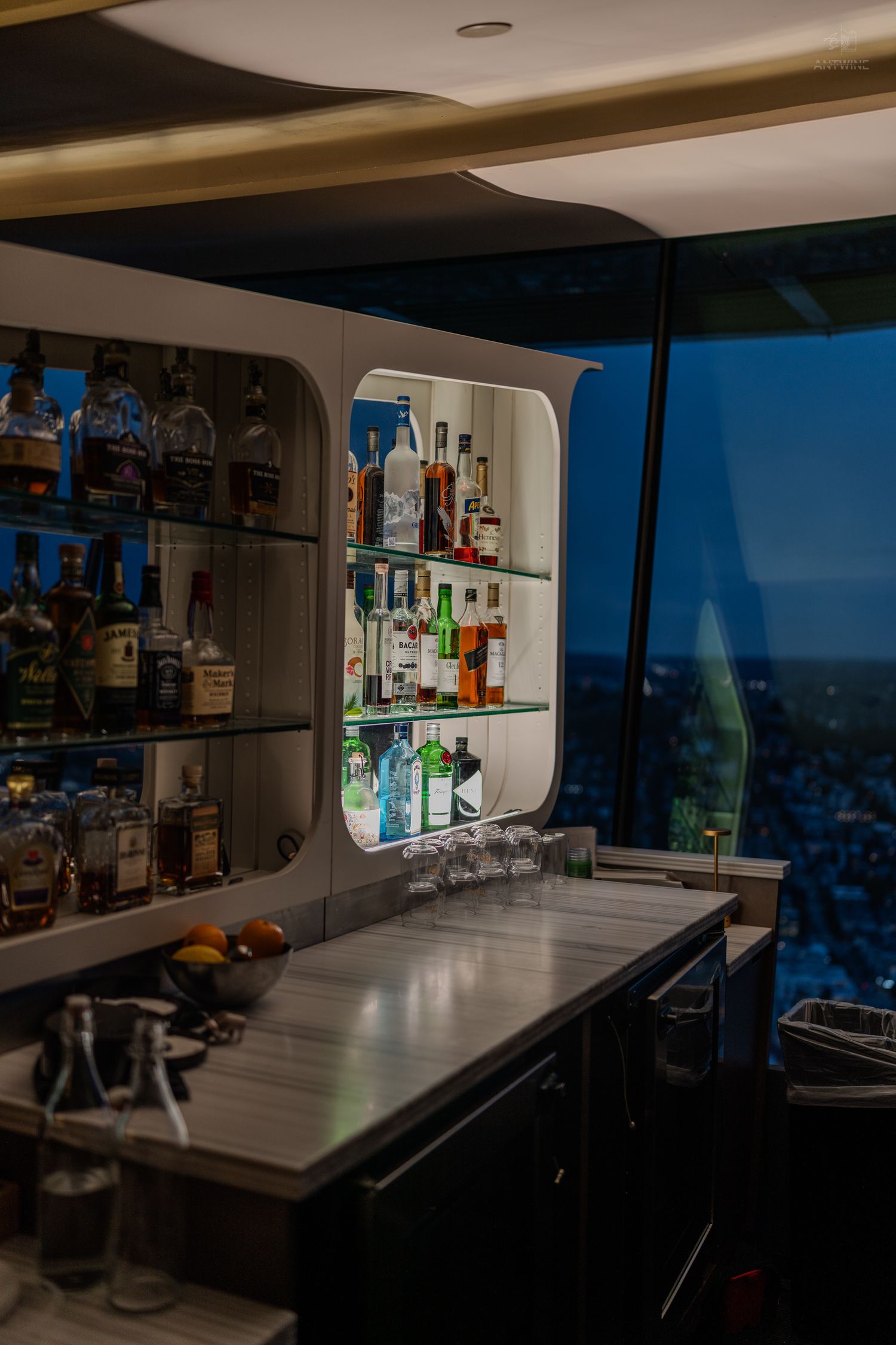 A dimly lit rooftop bar with shelves of liquor bottles and a city view at night.