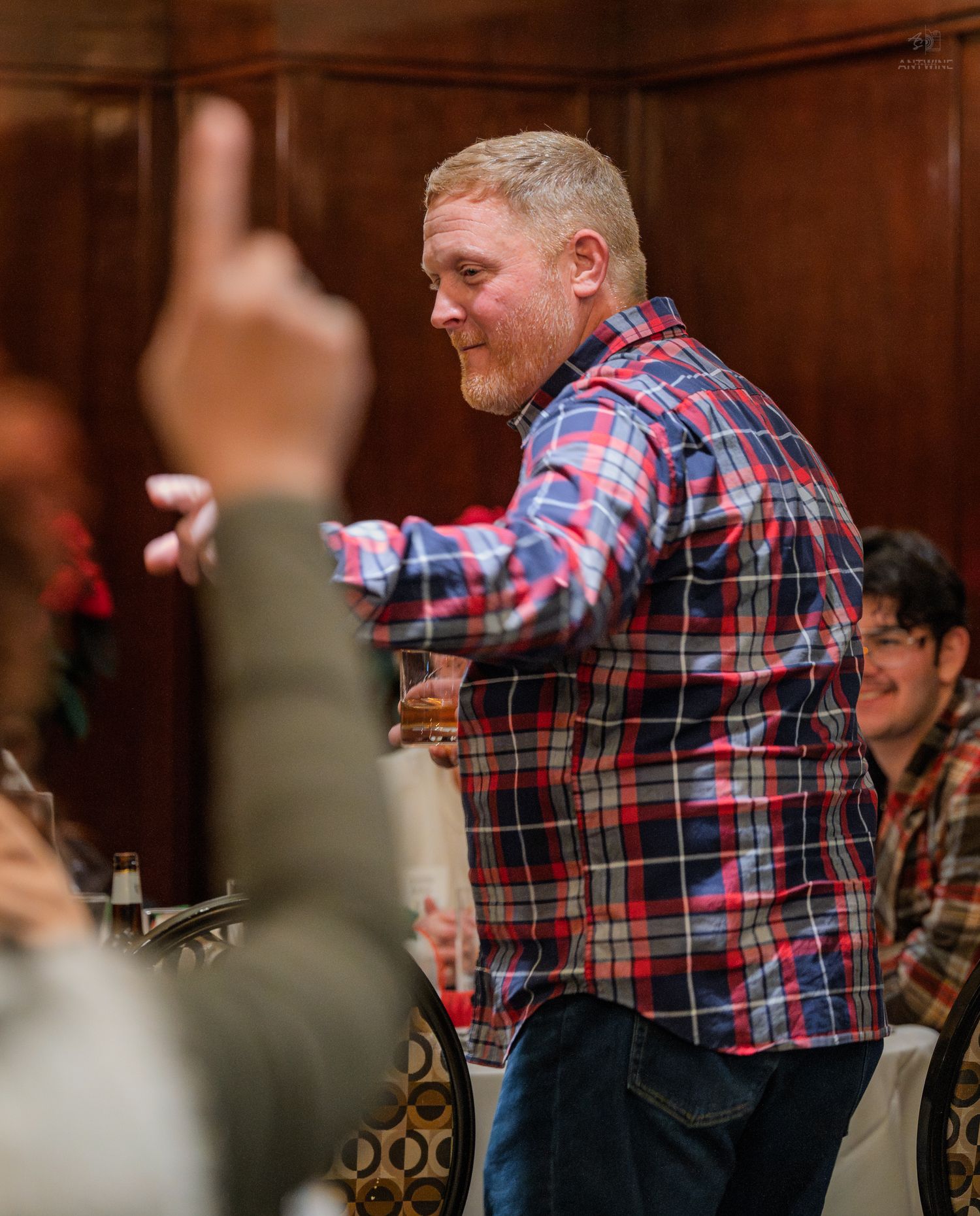 Smiling man in plaid shirt holding drink while standing at social gathering.
