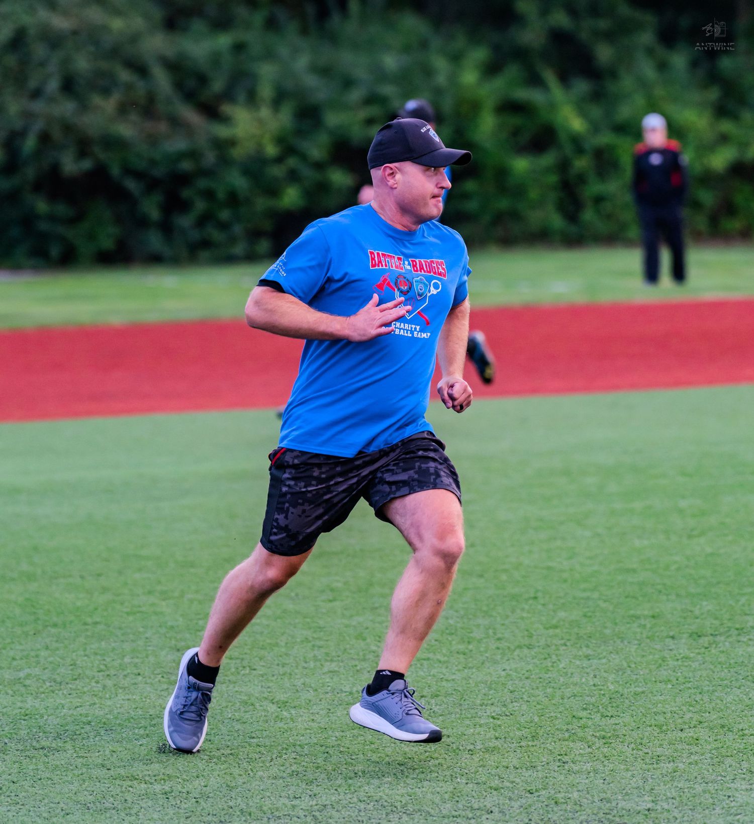 Athlete in blue graphic t-shirt running across green baseball field during warm-up drills.