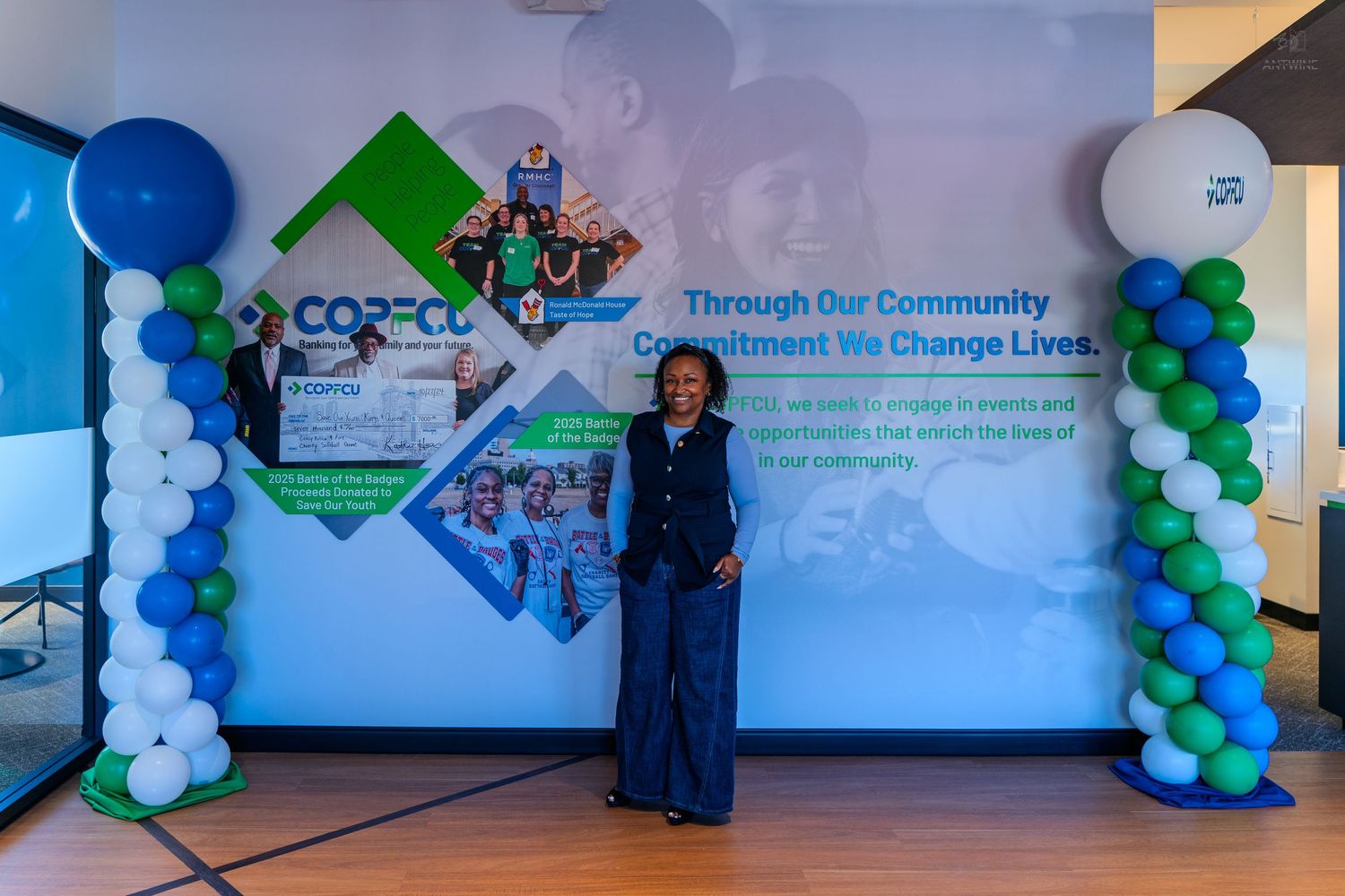 Woman stands before a COPECO community commitment banner with blue and green balloon columns at a corporate event.