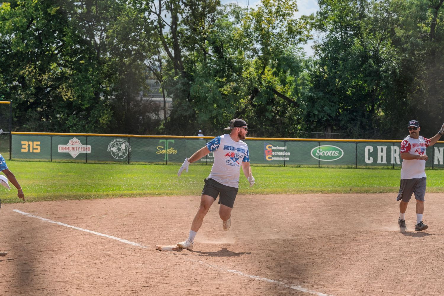 Baseball player rounding third base during an outdoor game on a sunny day.