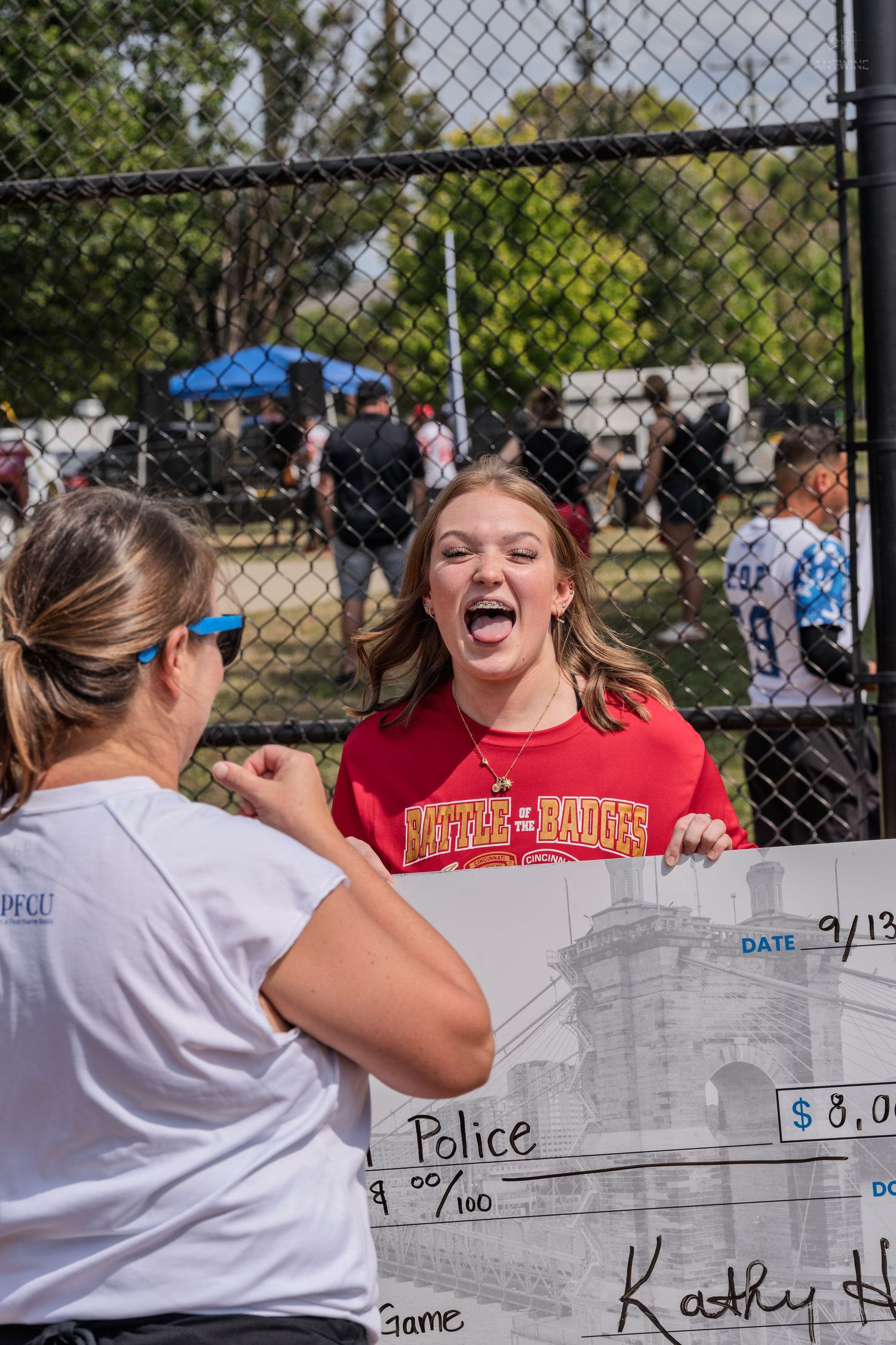 Excited girl reacting to large police charity check at outdoor softball fundraiser event.