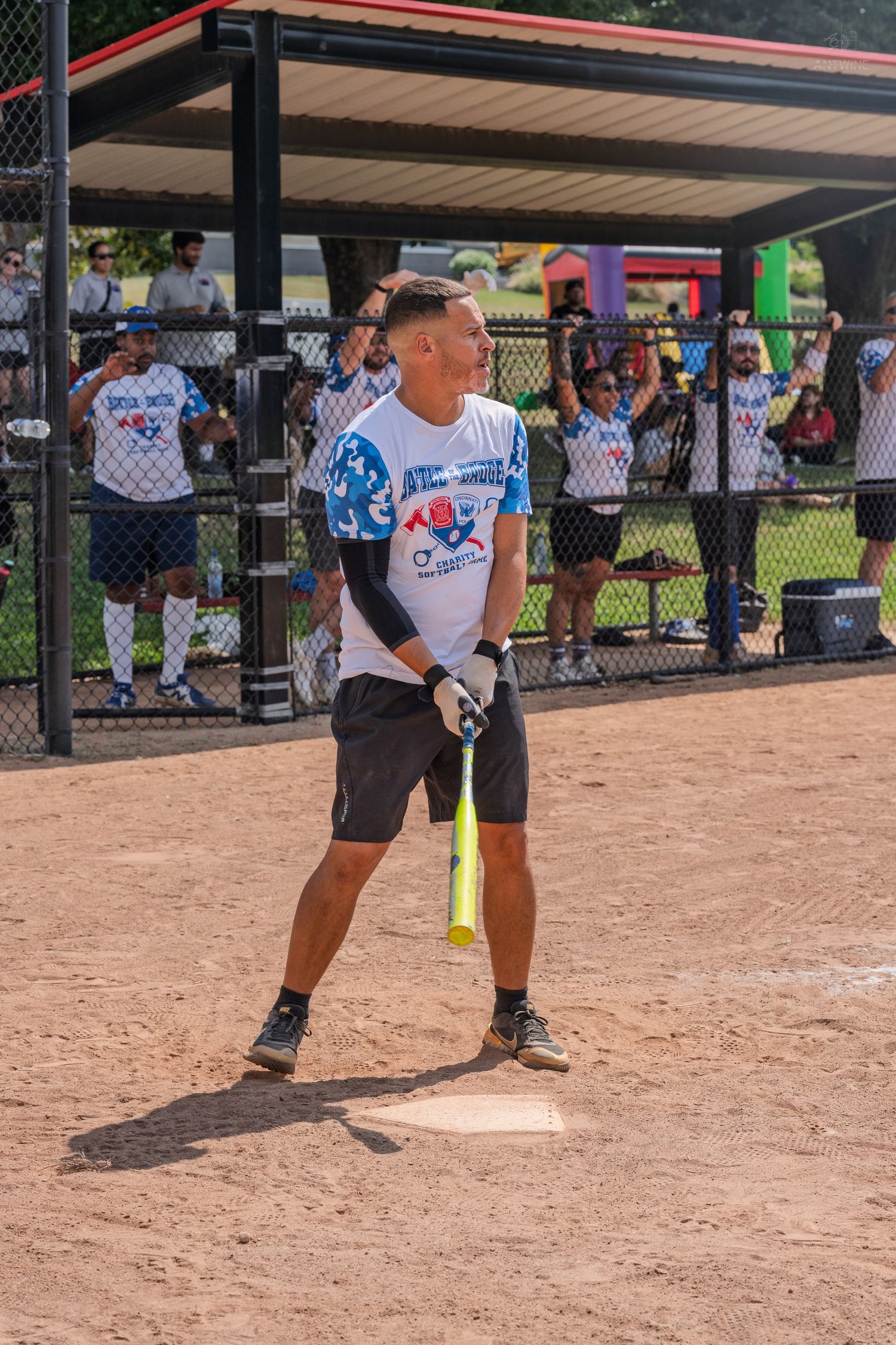 Male softball player in graphic jersey holding yellow bat at home plate during outdoor game.