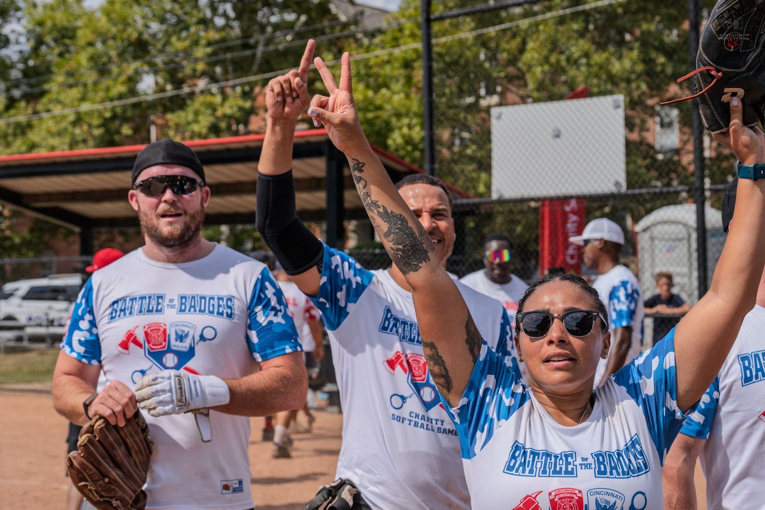 Excited Battle of the Badges softball players celebrate with raised hands on an outdoor field.