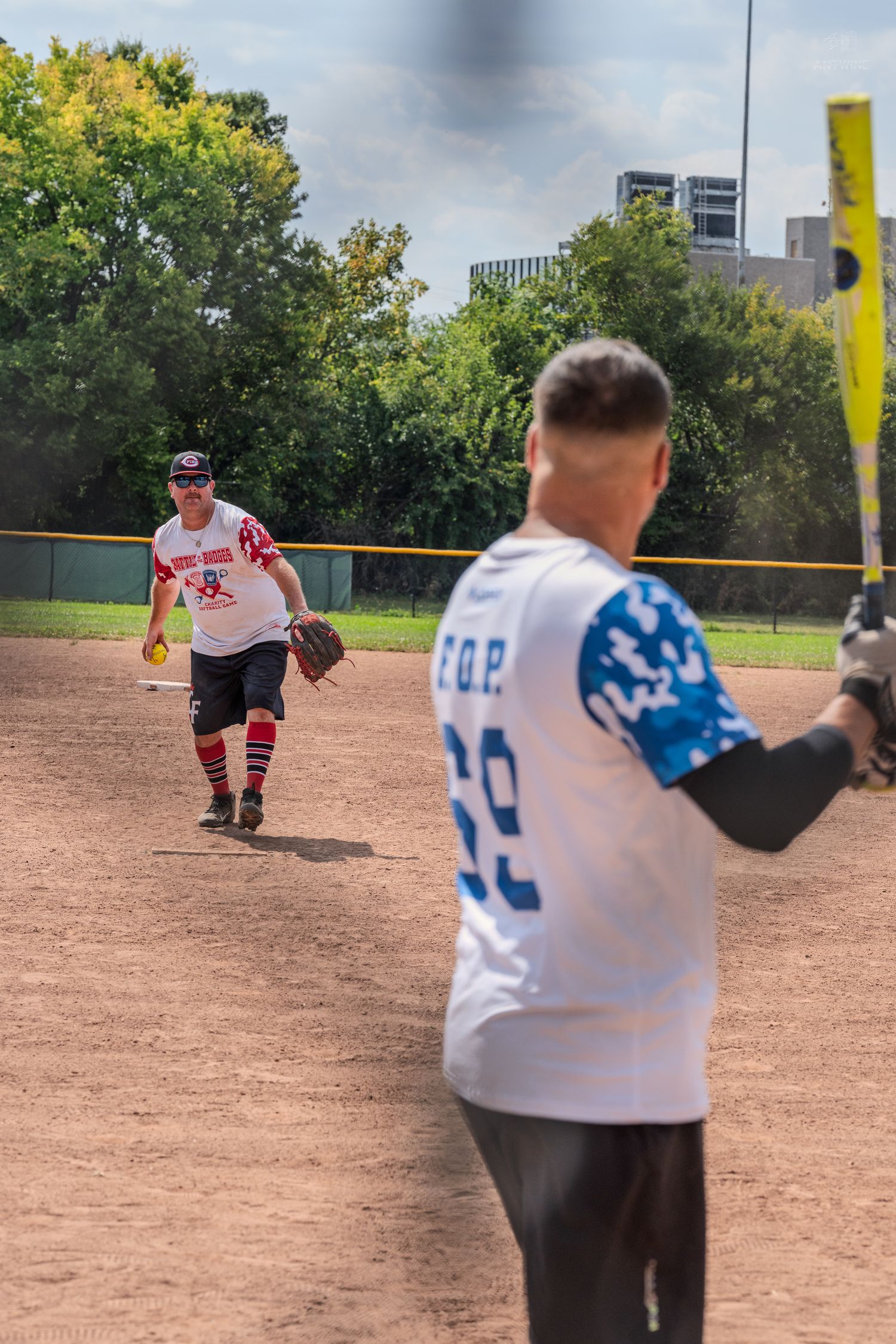 Softball pitcher winds up to throw as a F.O.P. #69 batter prepares at home plate on a sunny day.