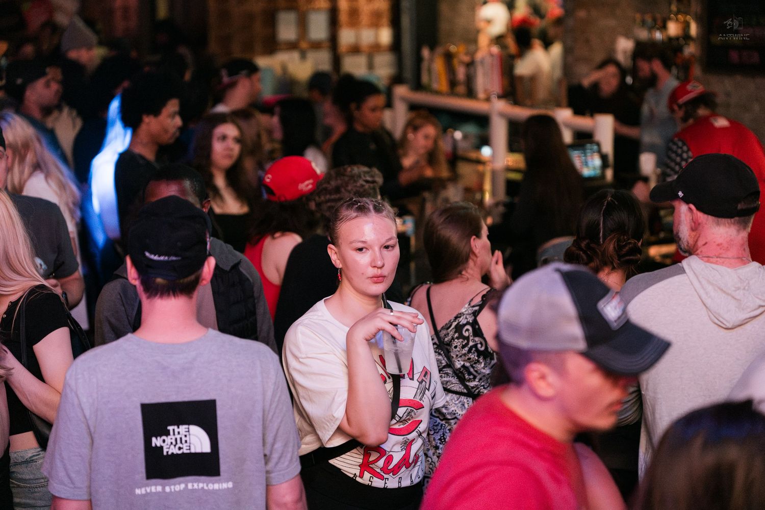 Crowded bar scene with young adults socializing and mingling indoors at a busy nightlife venue.