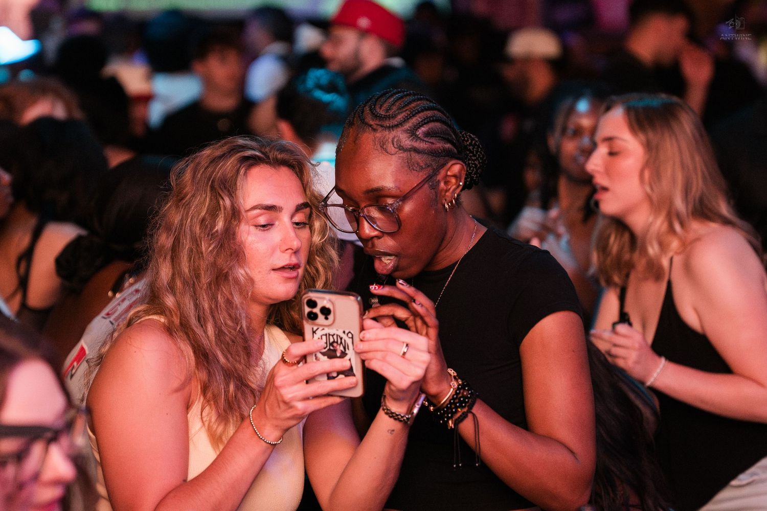 Two women looking at a smartphone together at a lively nightclub event.