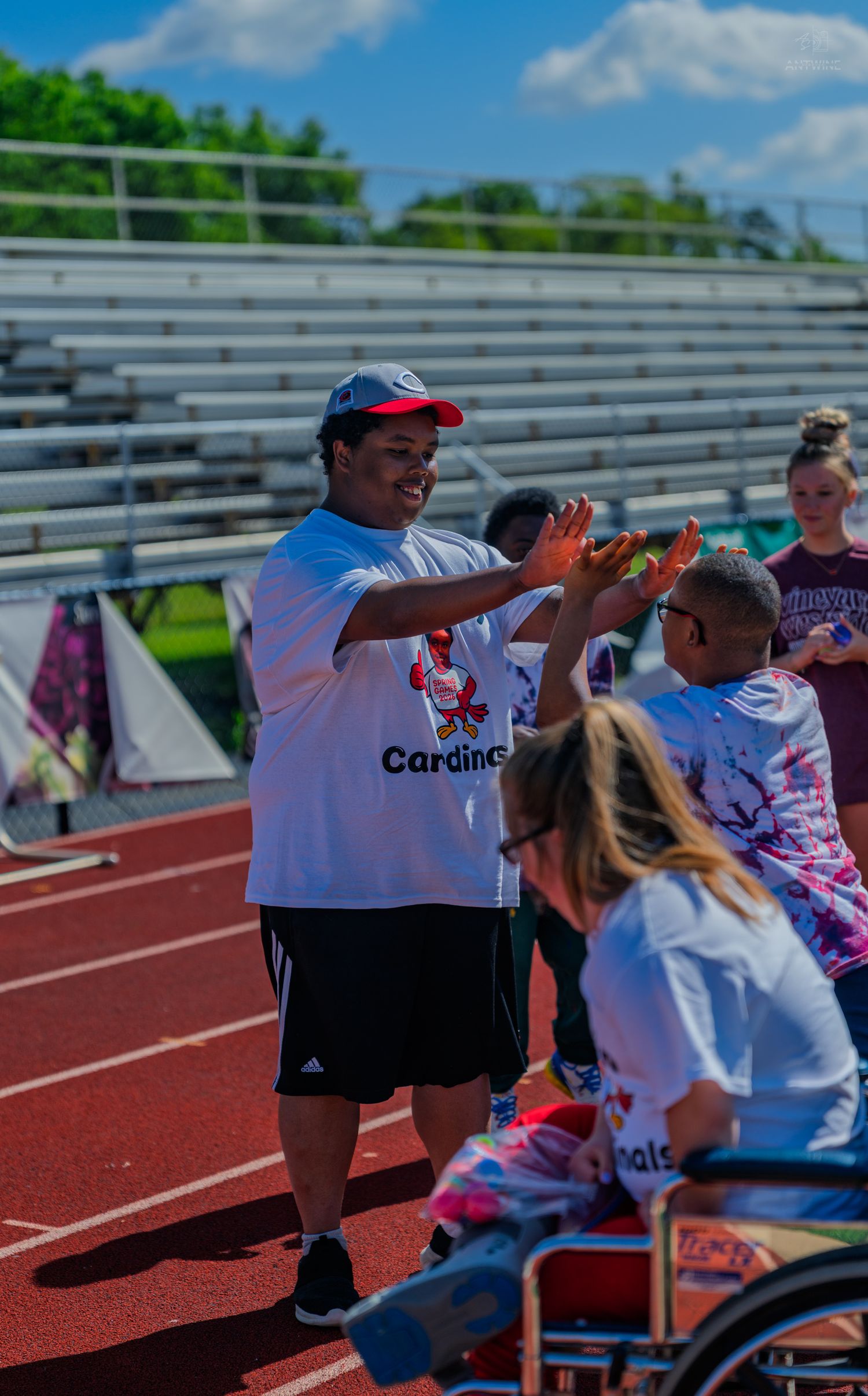 Students in Cardinals shirts high-five on a red track during a special needs athletic event on a sunny day.