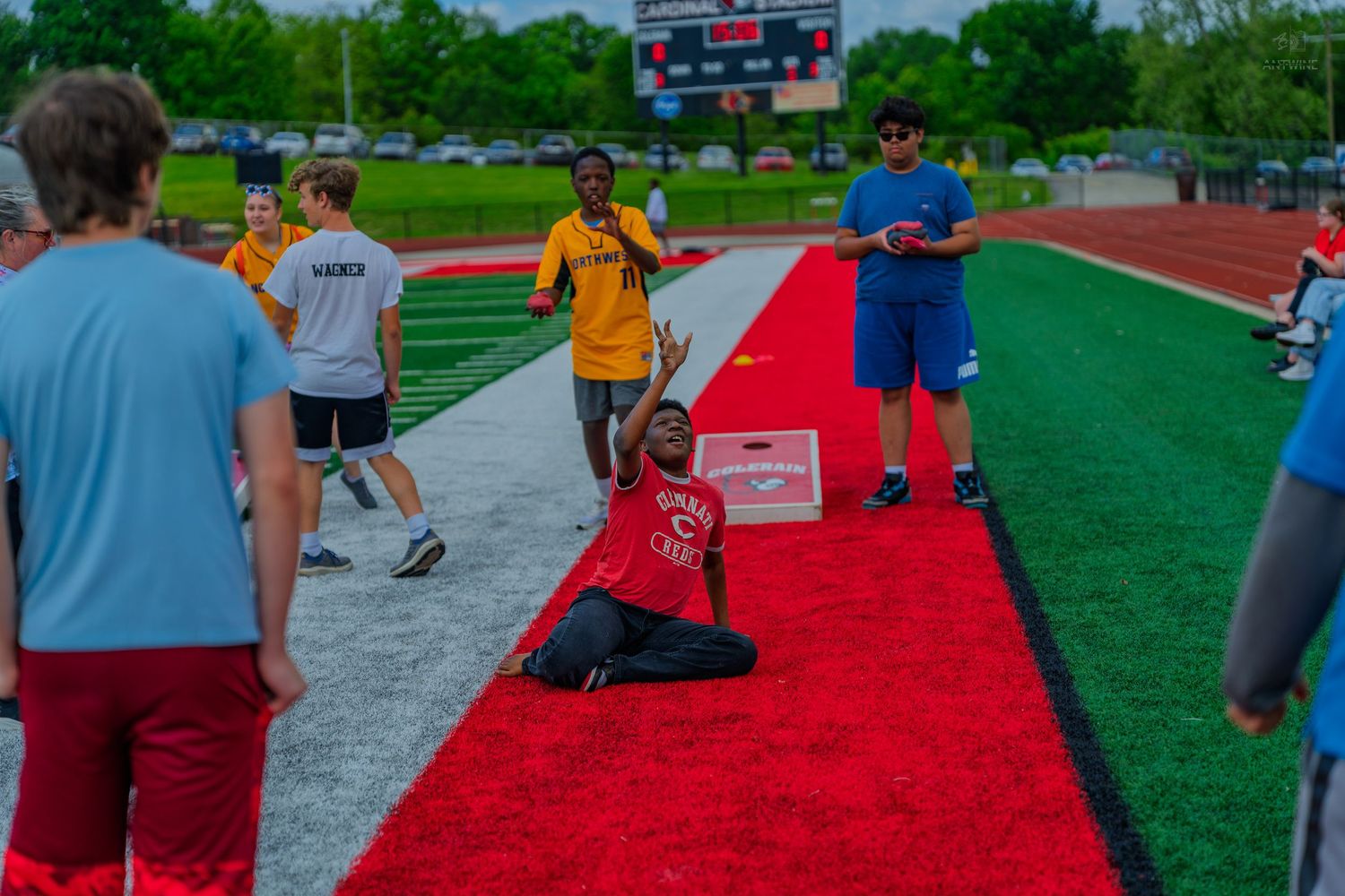 Athletes compete in long jump event on red track at outdoor stadium during a sunny day track meet.